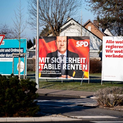 Mehrere Ständer mit Wahlplakaten stehen nebeneinander an einer Grünfläche.