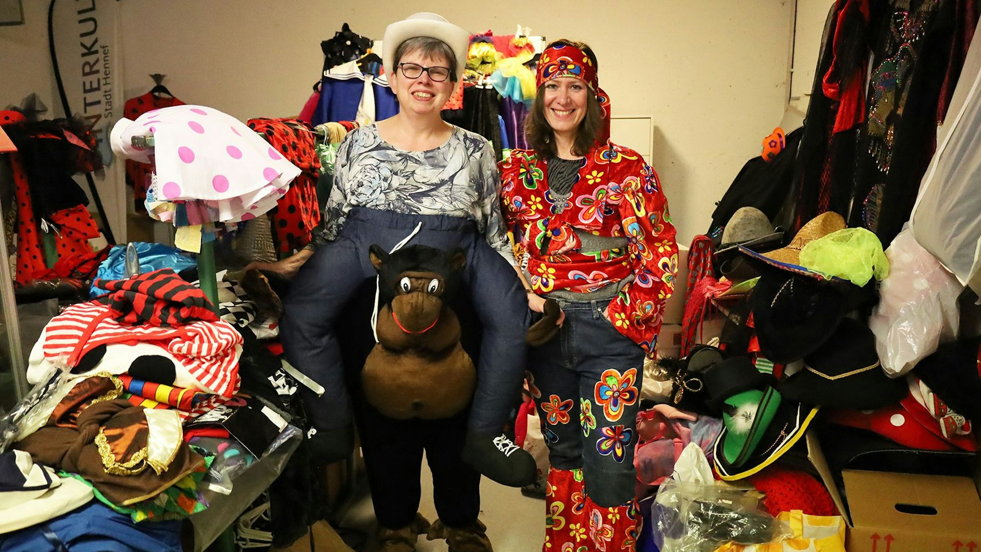 Zwei Frauen stehen in Karnevalskostümen zwischen vielen weiteren Kostümen.