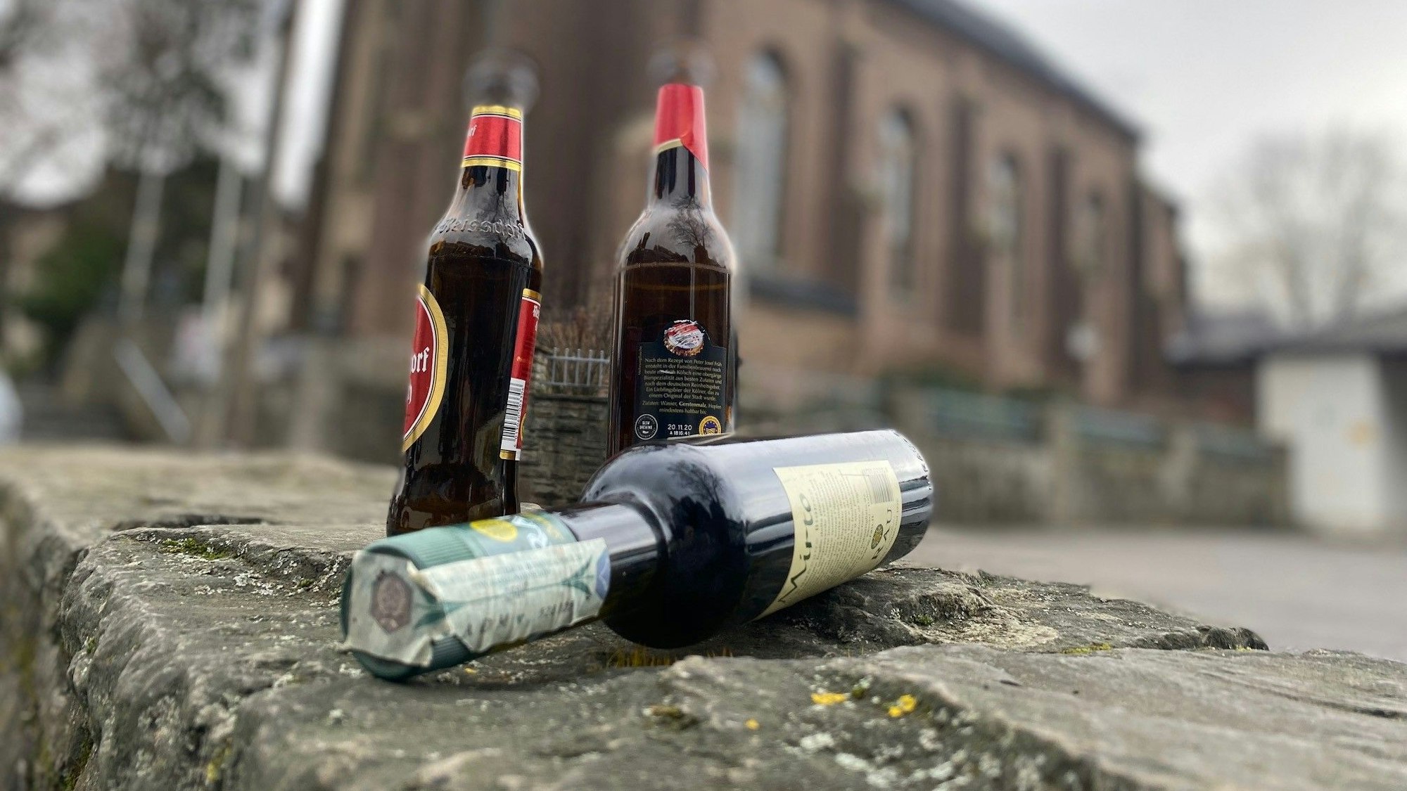 Auf dem Foto sind Bierflaschen und eine Weinflasche vor einer Kirche zu sehen.