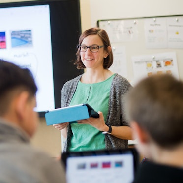Eine Lehrerin steht mit einem iPad vor einer digitalen Schultafel im Englischunterricht einer 5. Klasse.