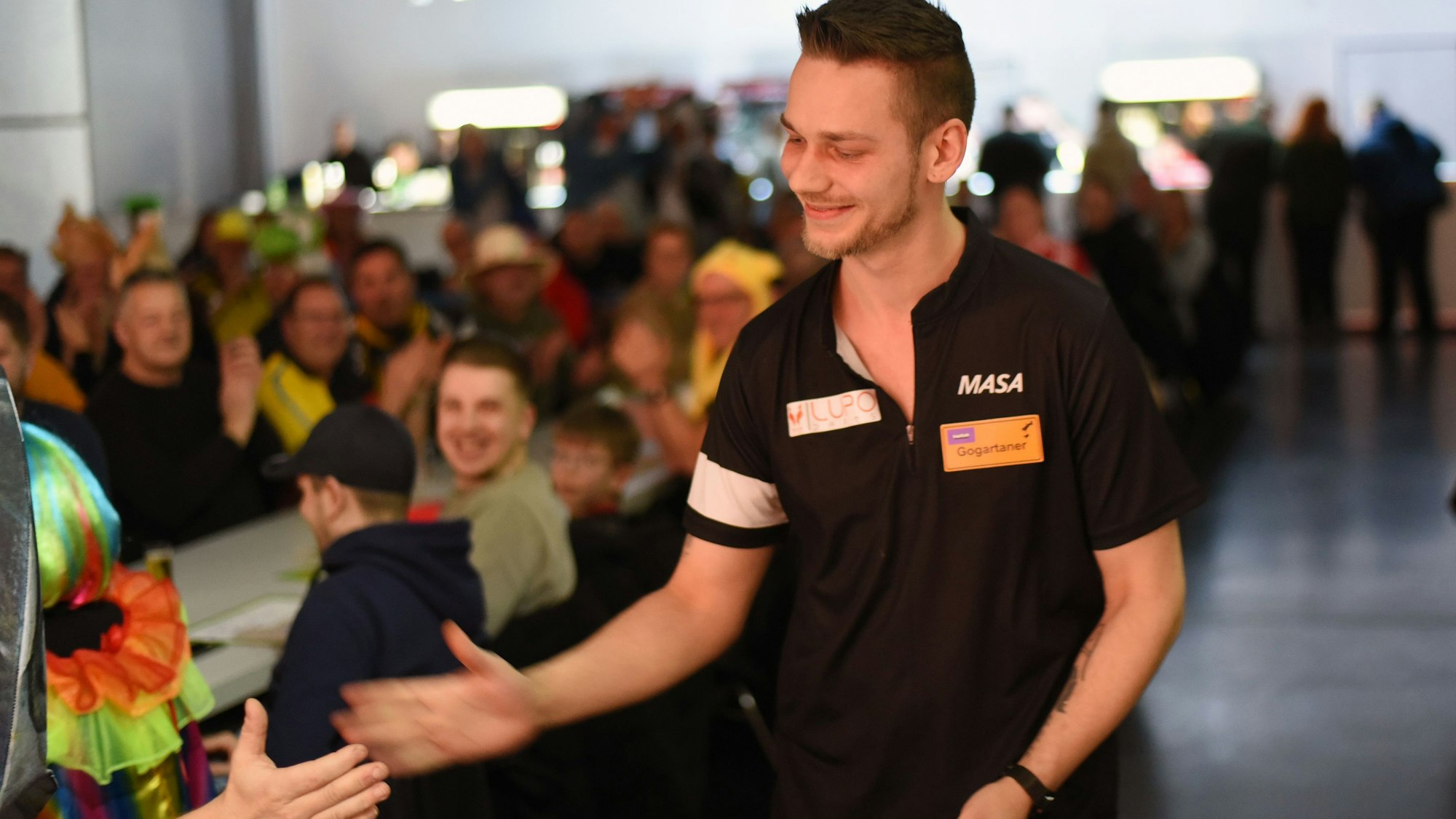 Zu sehen ist ein Dartspieler auf dem Weg durch das Publikum zur Bühne.