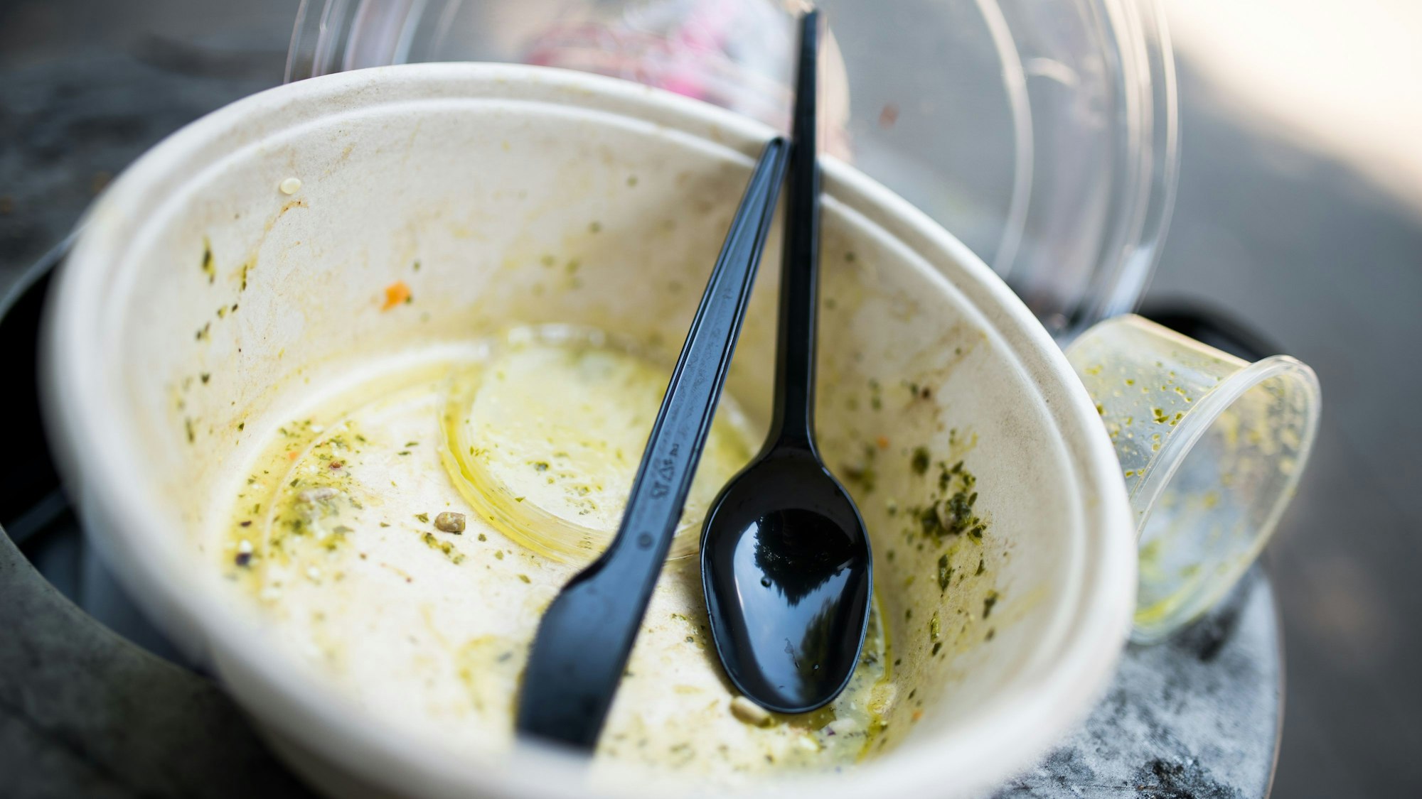 Gebrauchtes Plastikgeschirr liegt auf einem Mülleimer.