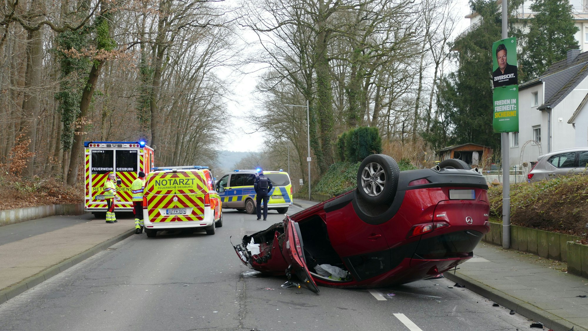 Ein rotes Auto liegt nach einem Unfall auf dem Dach auf einer Straße in Siegburg.