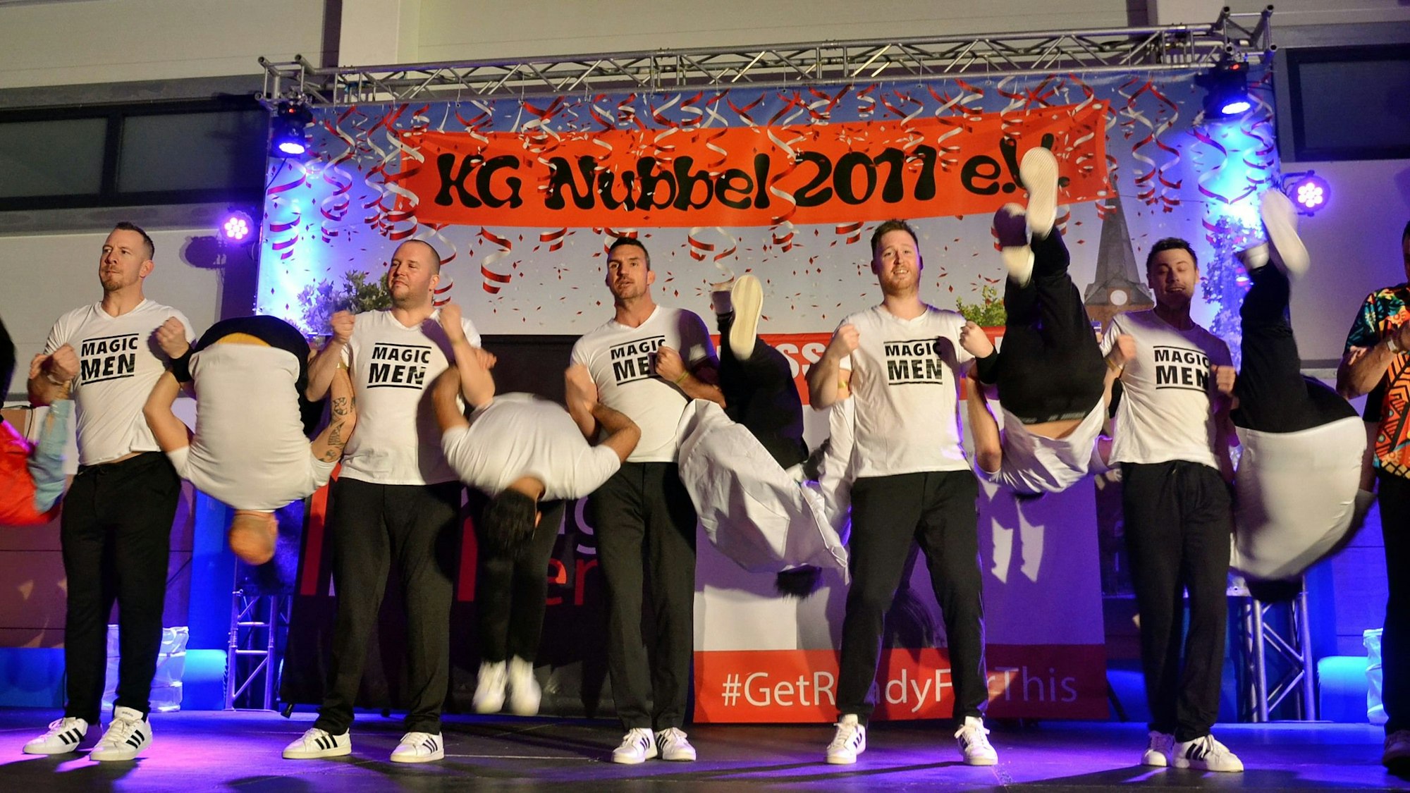 Das Männerballett Magic Men steht auf der Bühne und führt seine Choreografie vor. Im Hintergrund hängt ein Banner der KG Nubbel 2011.
