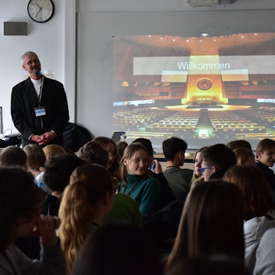 Ein Mann steht neben einer Präsentation vor jungen Menschen.