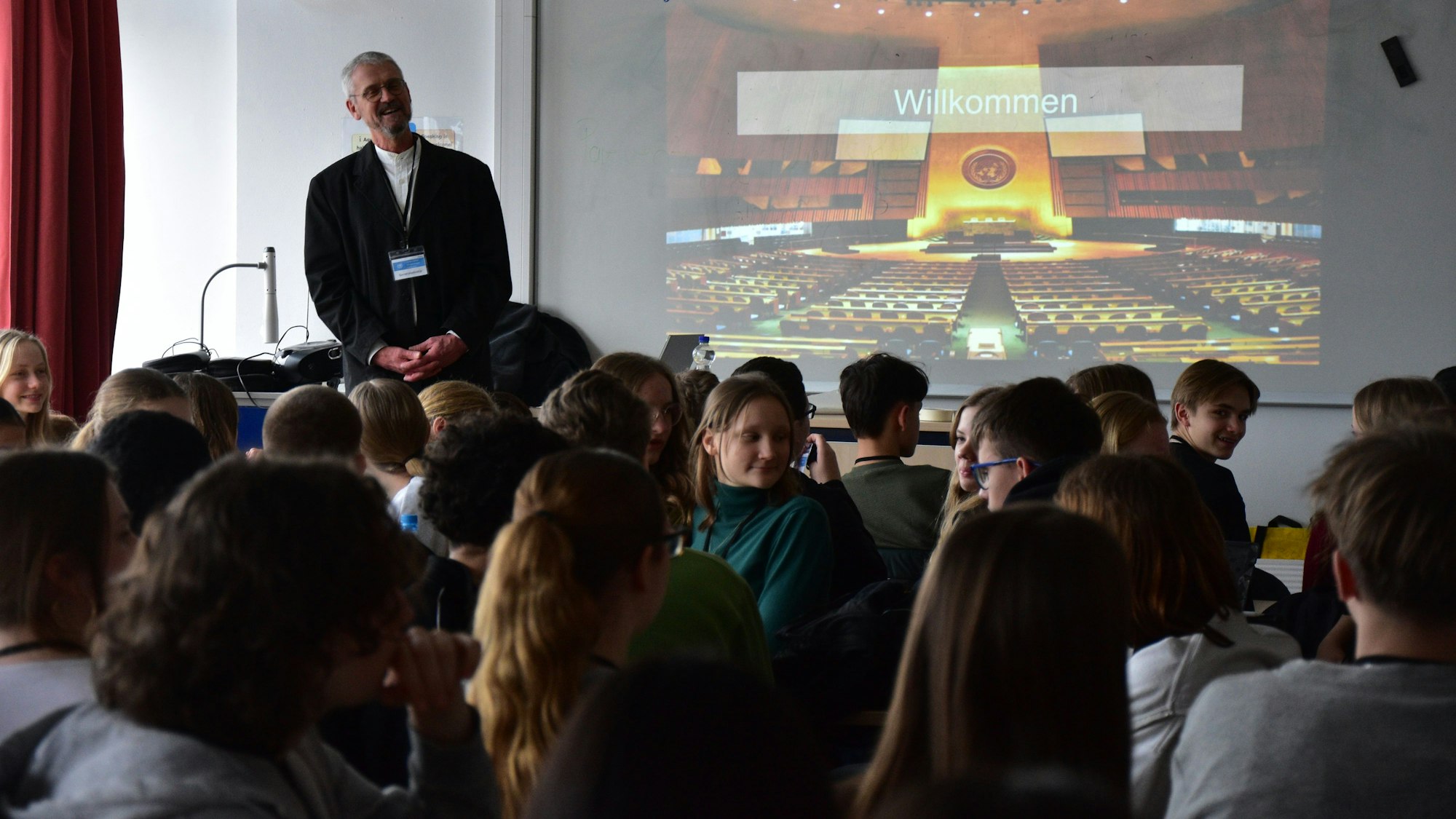 Ein Mann steht neben einer Präsentation vor jungen Menschen.