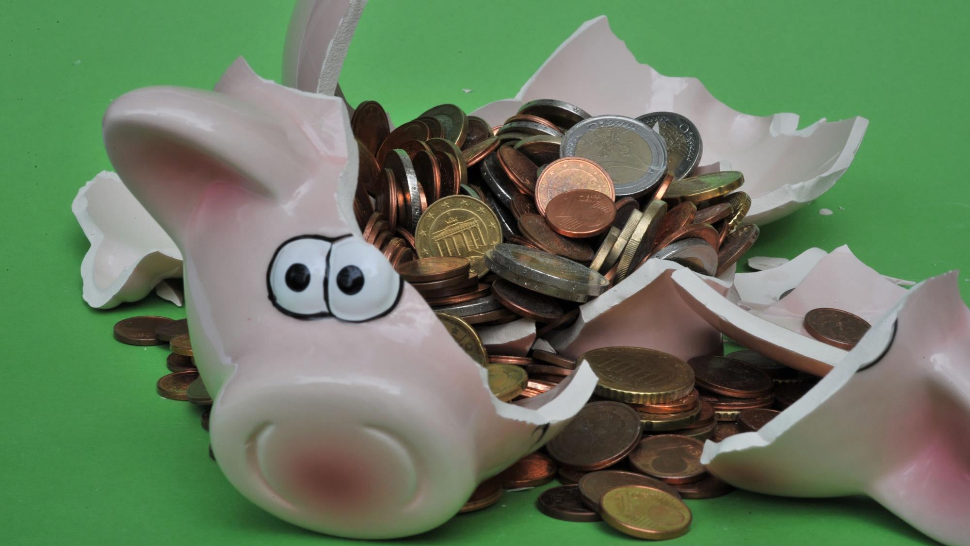 Ein Sparschwein mit Euro-Geldstücken liegt zerbrochen auf einem Tisch.