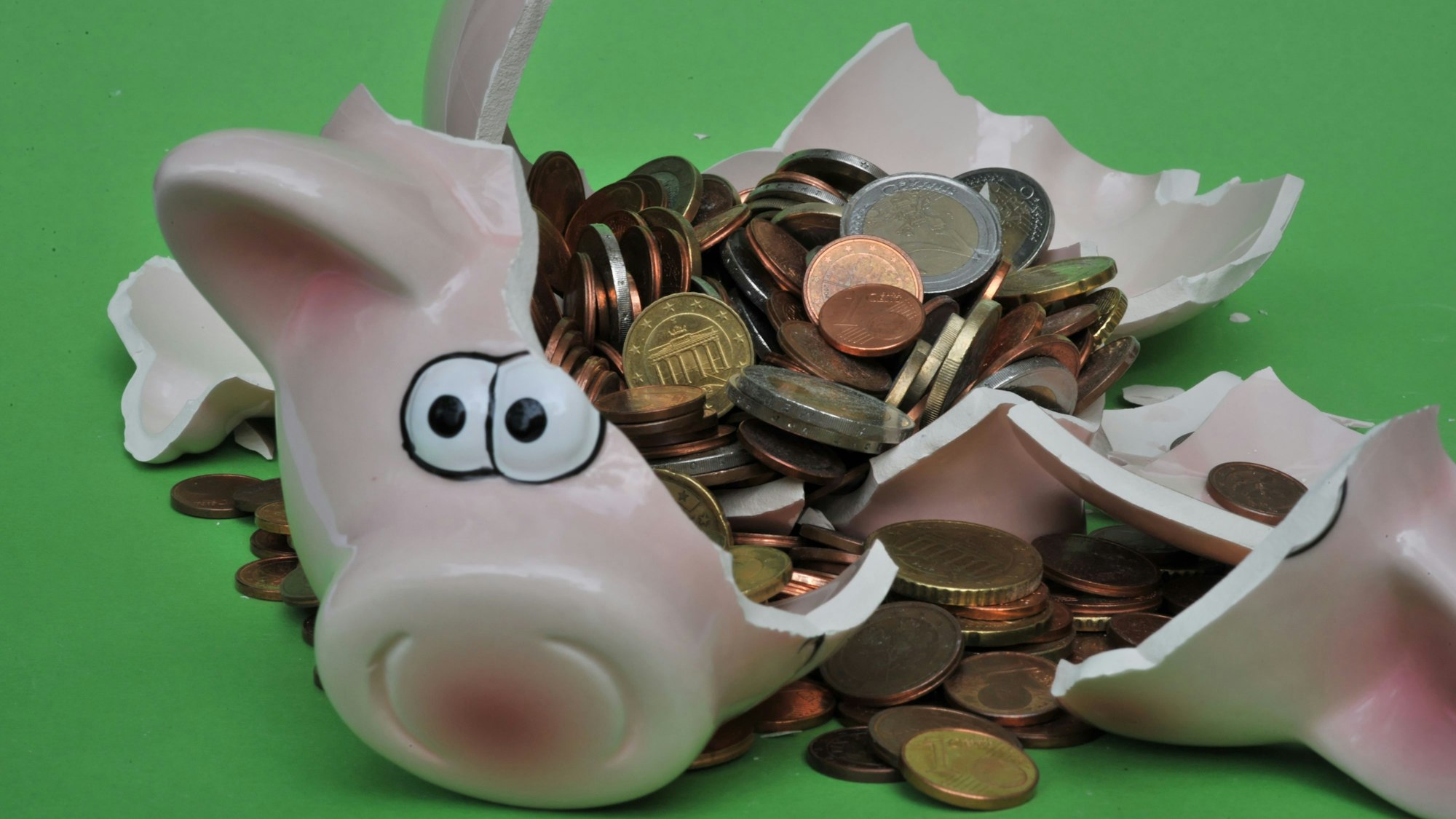 Ein Sparschwein mit Euro-Geldstücken liegt zerbrochen auf einem Tisch.