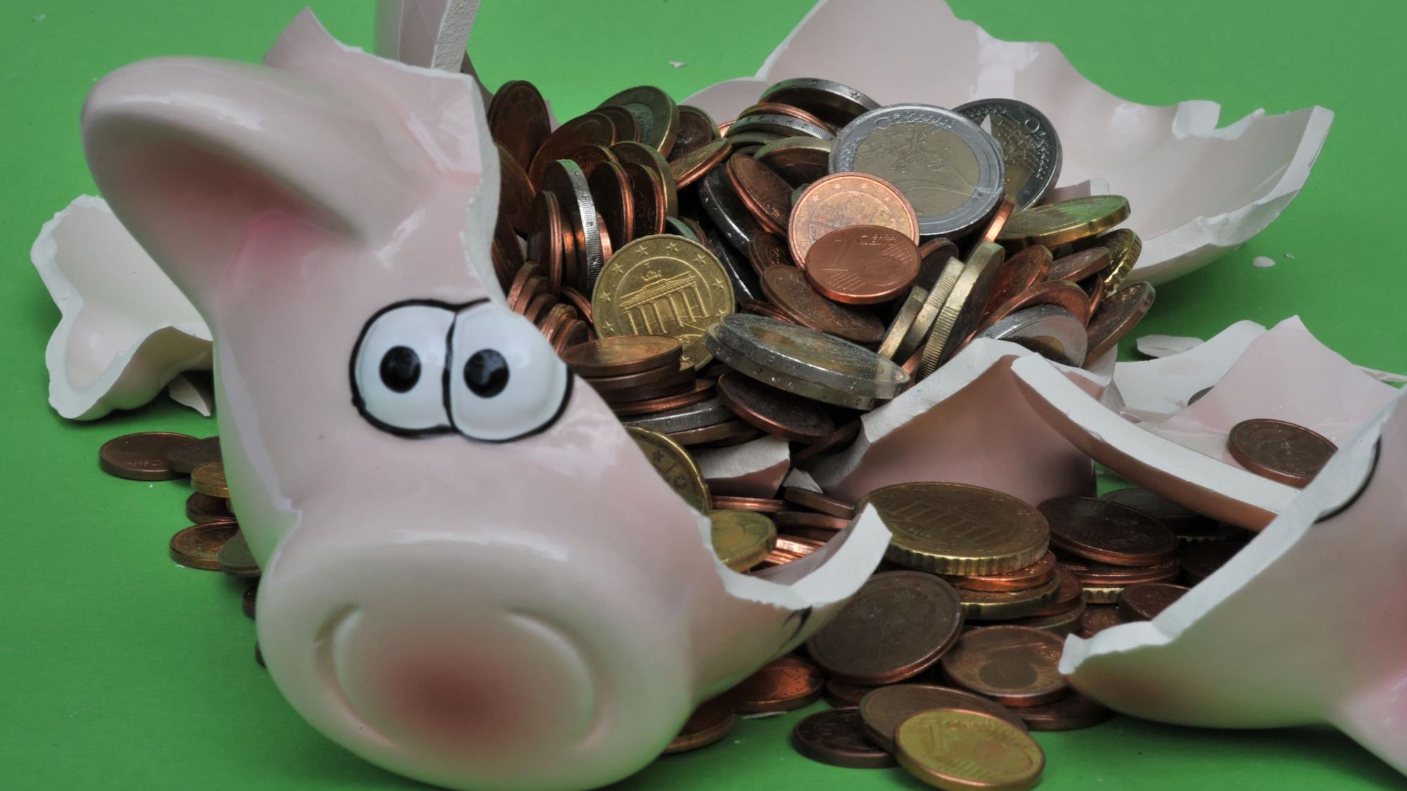 Eine Sparschwein mit Euro-Geldstücken liegt zerbrochen da.