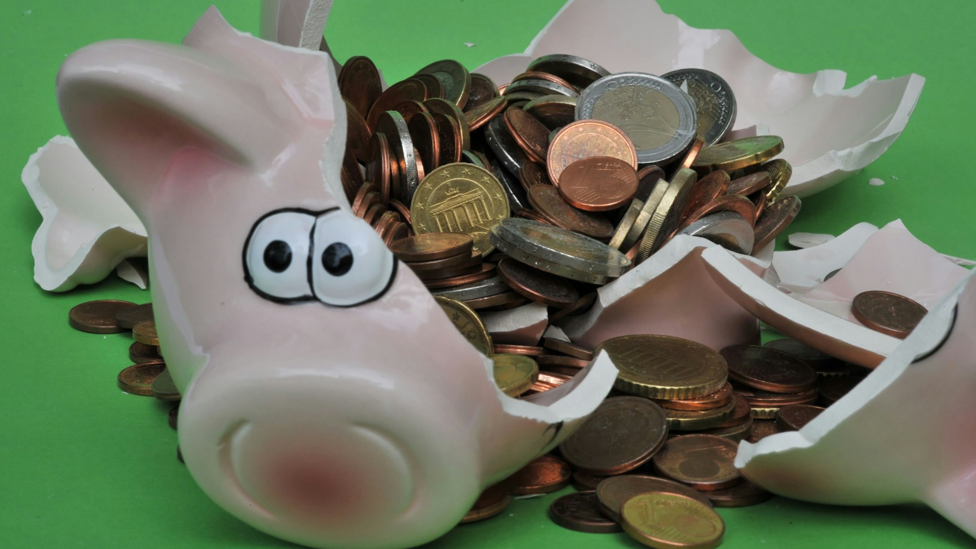 Eine Sparschwein mit Euro-Geldstücken liegt zerbrochen da.