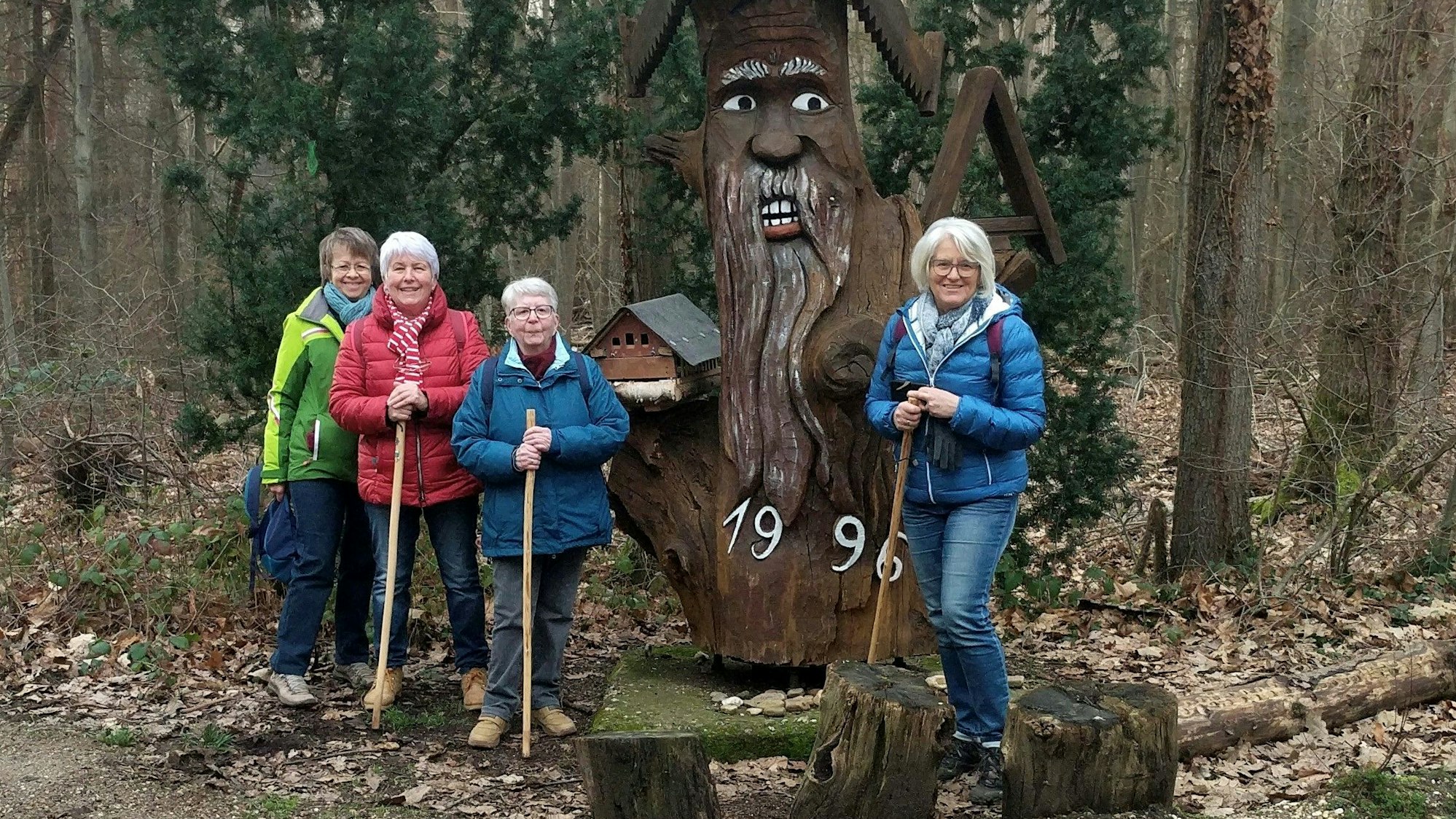 Vier Wanderinnen stehen am Hölzernen Mann auf der Eifelspur „Zwischen Ville und Eifel“ im Wald bei Weilerswist.