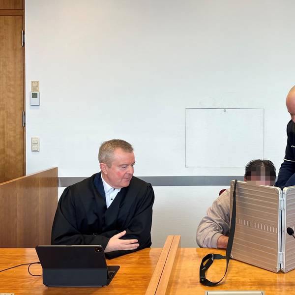 Der Angeklagte wird von einem Justizbediensteten in den Sitzungssaal des Bonner Landgerichts gebracht. Er verbirgt sein Gesicht hinter einem silberfarbenen schmalen Koffer, neben ihm sitzt sein Anwalt in schwarzer Robe.