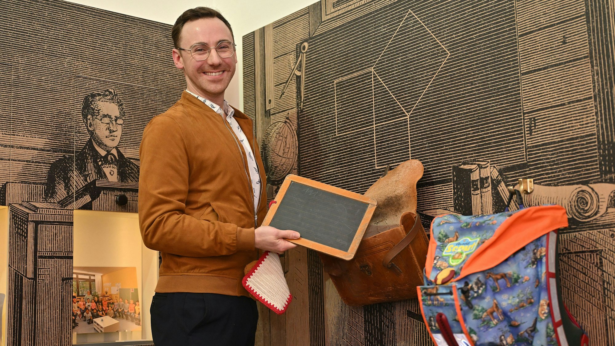 Ein junger Mann hält eine Schiefertafel in der Hand und lächelt.