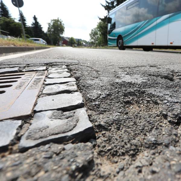 Schlaglöcher auf einer Straße, an denen gerade ein Linienbus vorbeifährt.