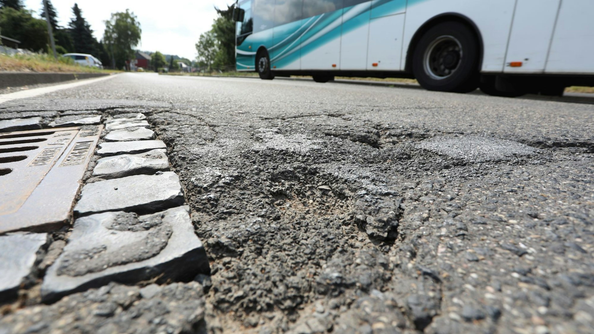 Schlaglöcher auf einer Straße, an denen gerade ein Linienbus vorbeifährt.