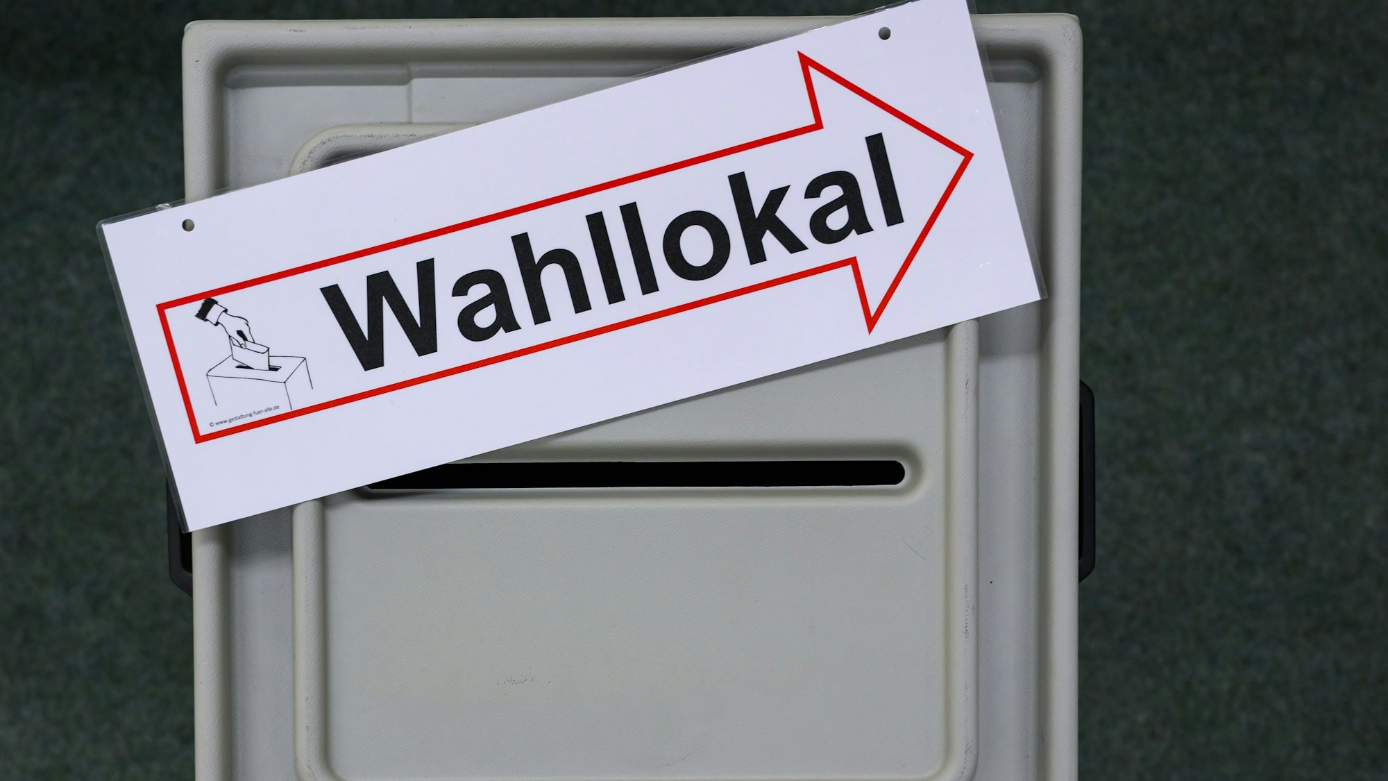 Ein Schild mit der Aufschrift Wahllokal liegt auf einer Wahlurne.