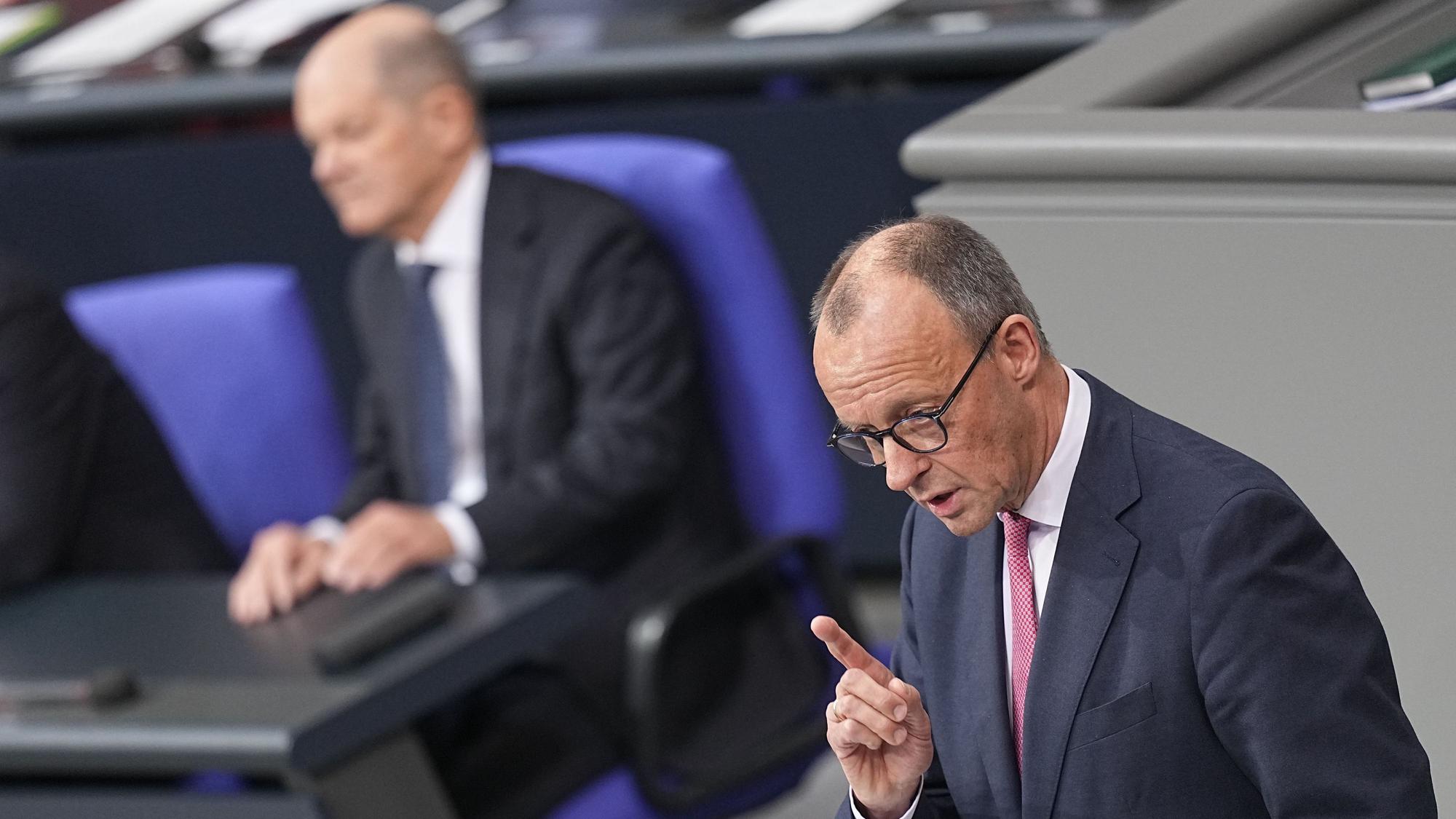 Bundeskanzler Olaf Scholz (SPD) hört Friedrich Merz (r), CDU Bundesvorsitzender und CDU/CSU Fraktionsvorsitzender im Bundestag, zu, als dieser bei der Debatte um das Zustrombegrenzungsgesetz im Plenarsaal im Bundestag spricht.