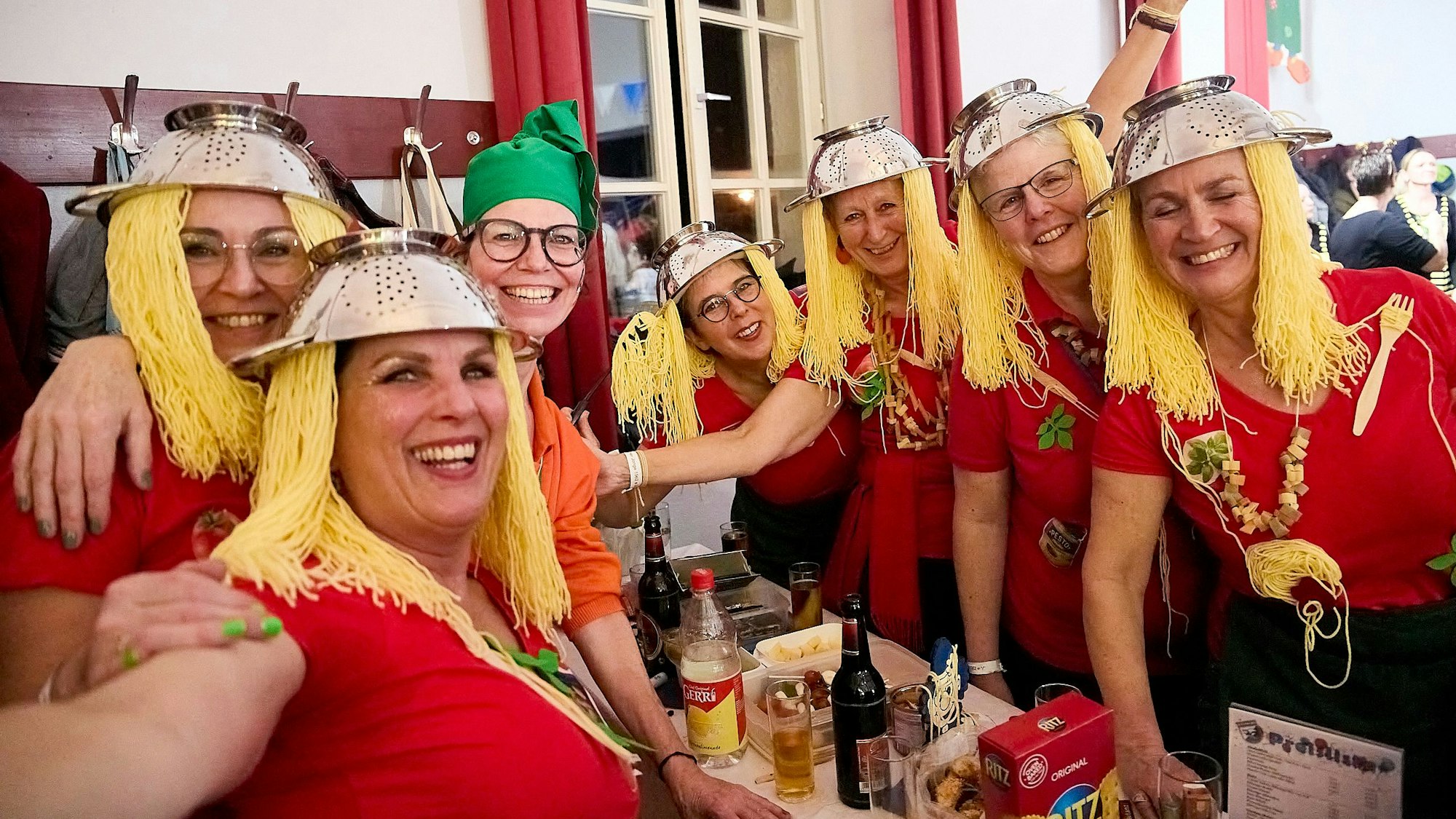 Eine Gruppe Frauen hat sich lustige Kostüme gebastelt: Zum tomatenroten Shirt tragen sie Nudelsiebe auf dem Kopf, die daran befestigten Fäden sehen aus wie Spaghetti.