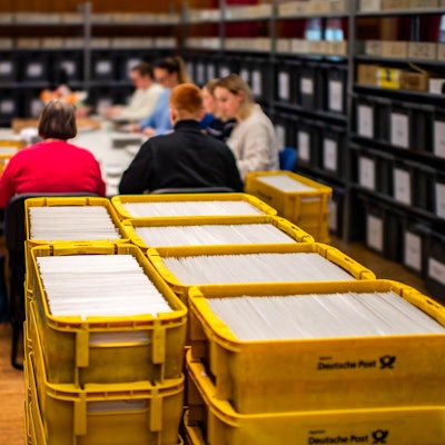 Das Bild zeigt einen Blick ins Wahlamt der Stadt Euskirchen. Im Vordergrund stehen zahlreiche gelbe Kisten mit Briefwahlunterlagen.