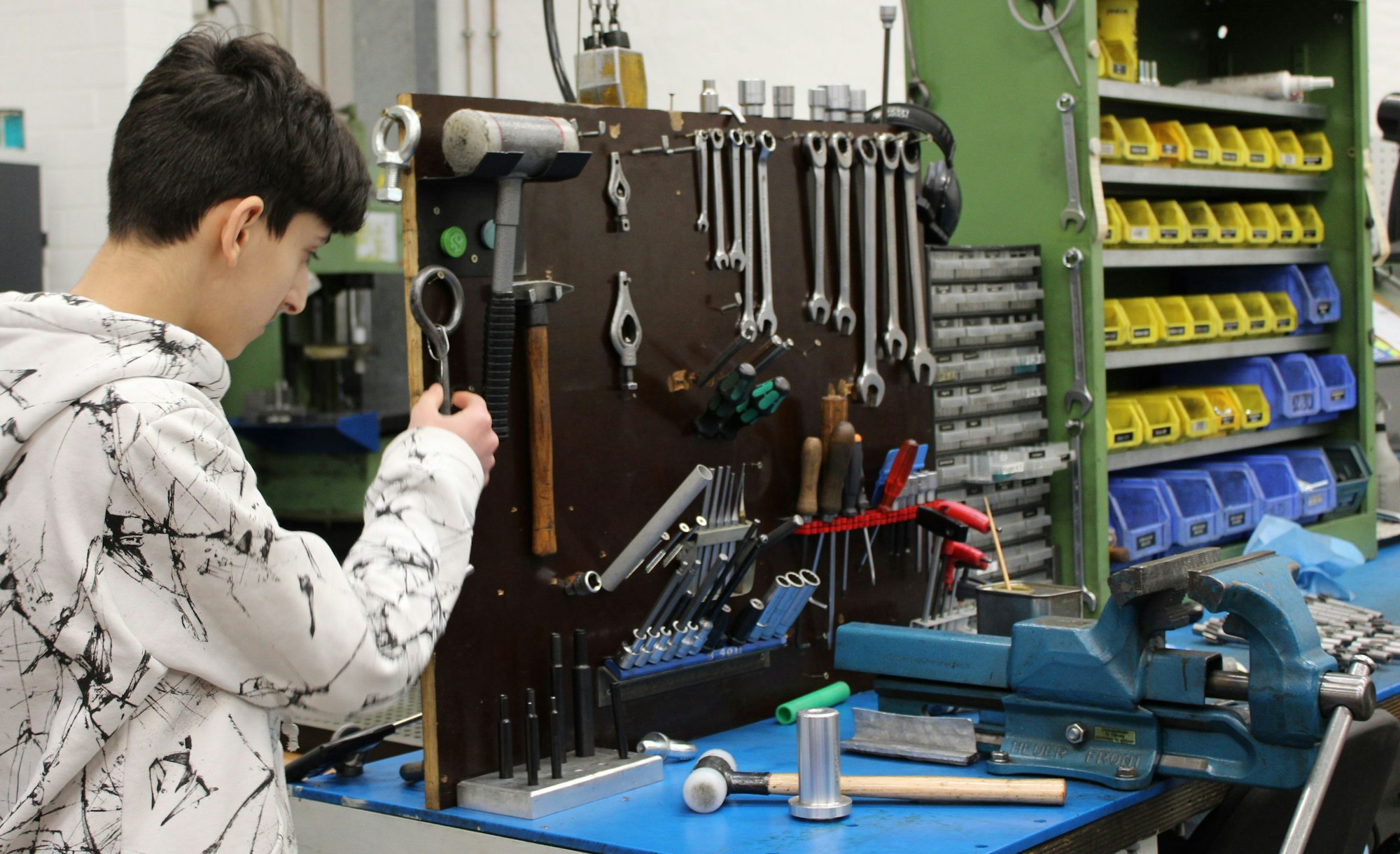 Ein Junge steht neben einem Tisch voller Werkzeug und schaut sich die einzelnen Gegenstände an.