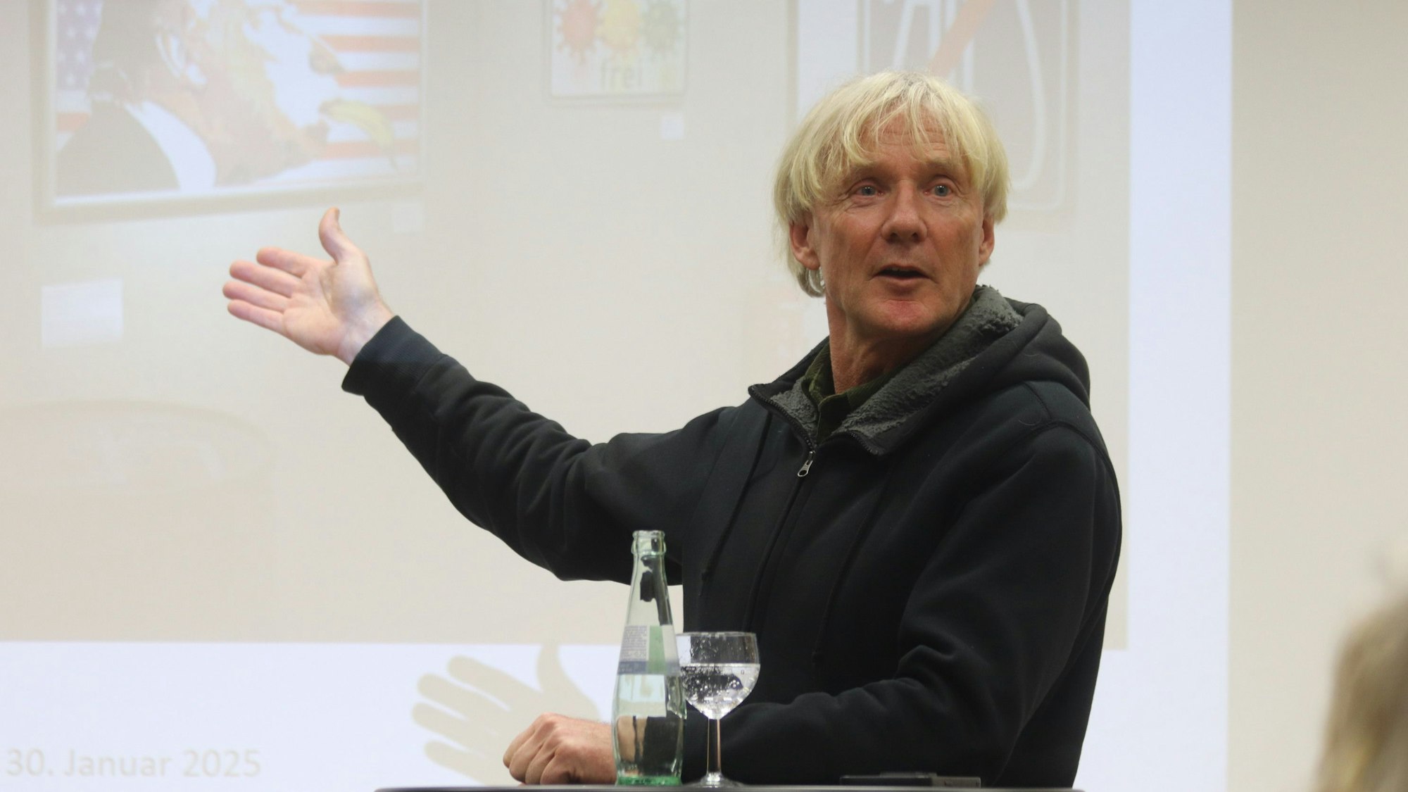 Der als Bananensprayer bekannte Thomas Baumgärtel steht gestikulierend vor einem an die Wand gebeamten Bild.