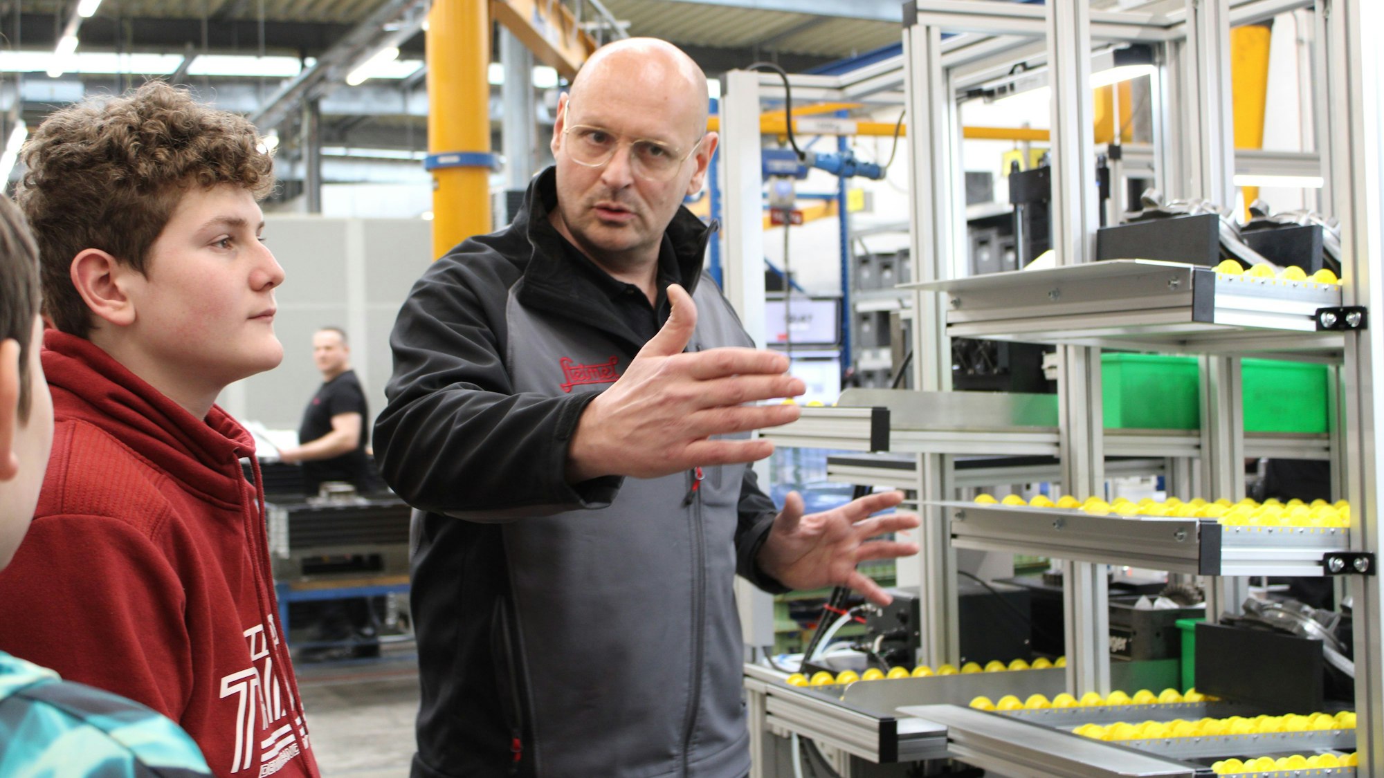 Ein Mitarbeiter gestikuliert, während er den neben sich stehenden Jungen etwas erklärt.
