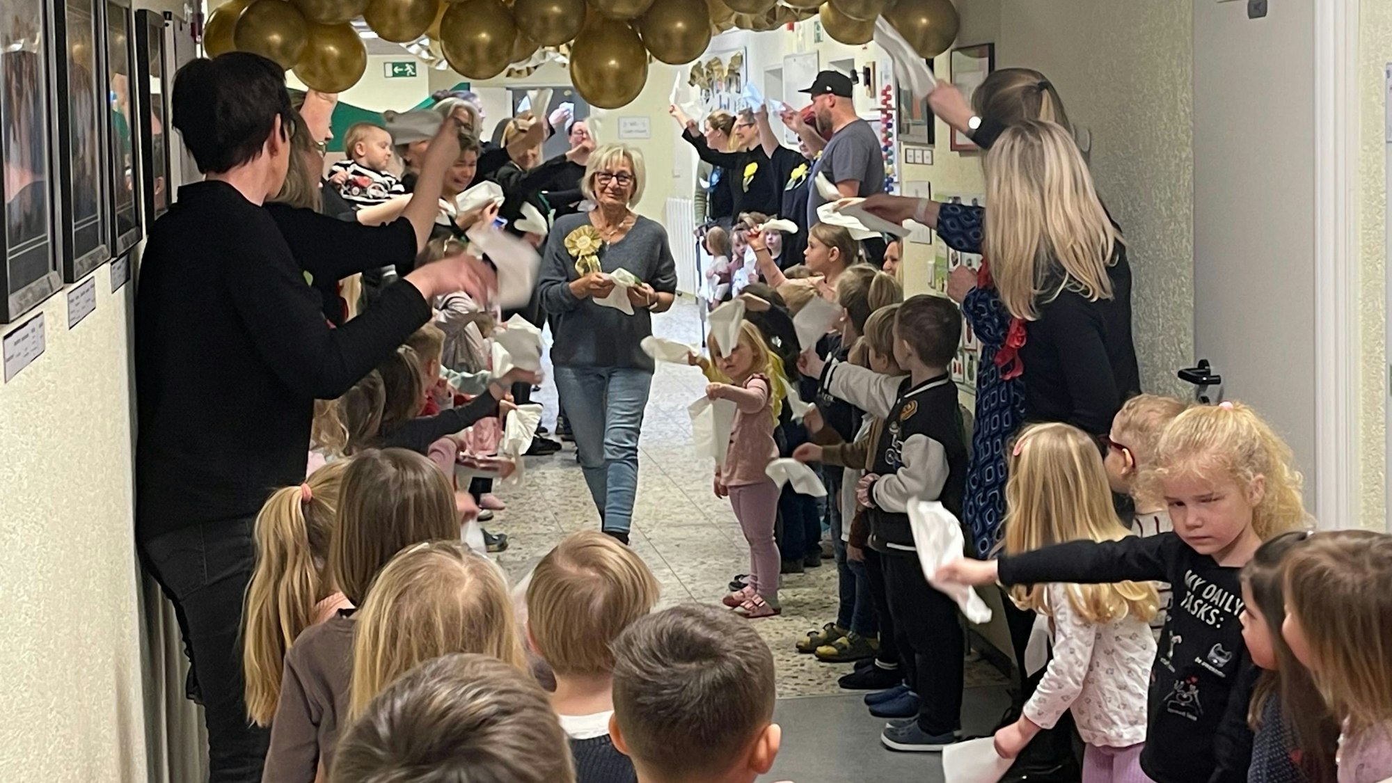 Zu sehen ist eine Frau, die durch ein Spalier von Kindern und Erwachsenen geht, die mit Taschentüchern winken.