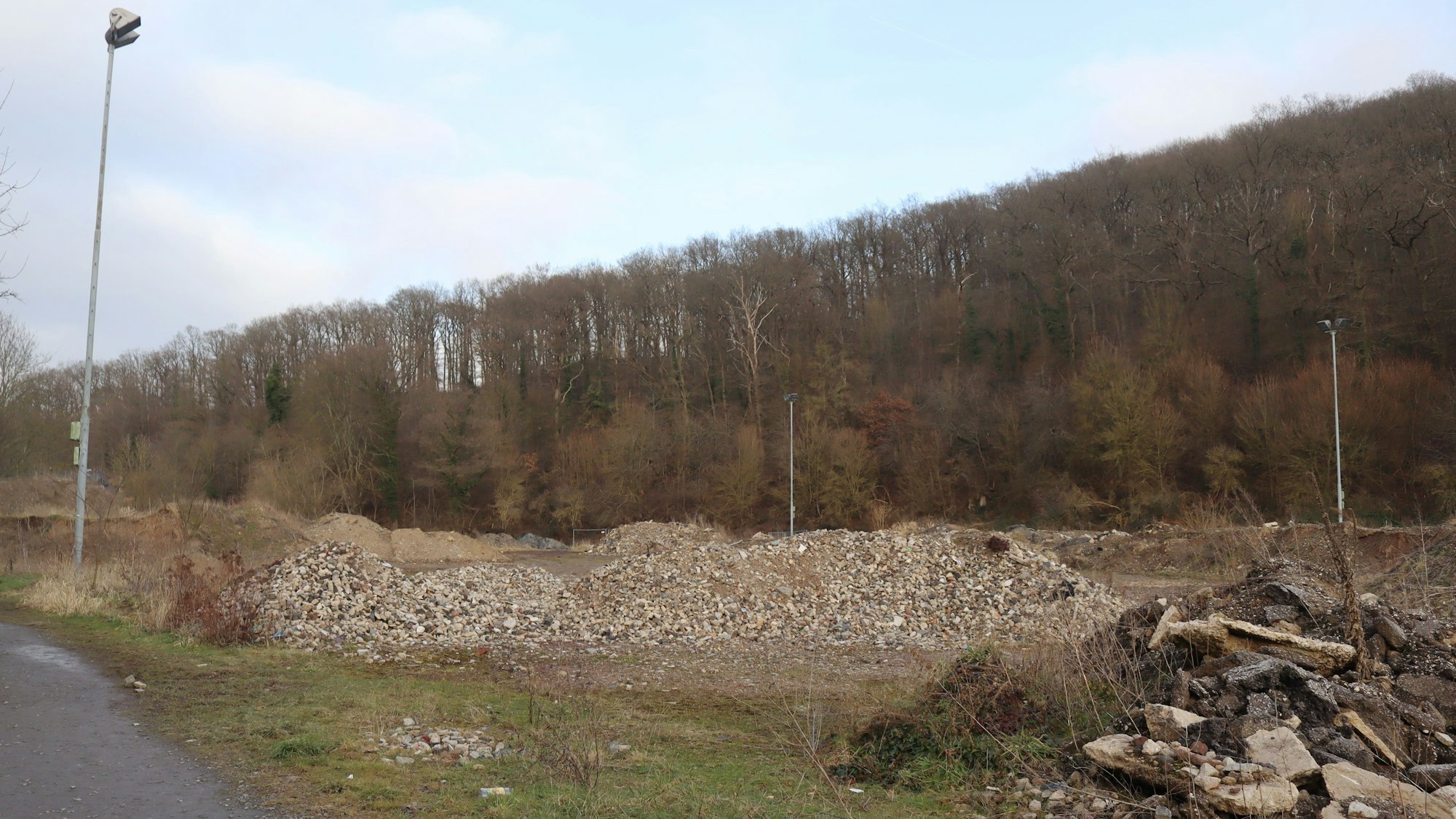 Auf dem früheren und zukünftigen Sportplatz liegt Geröll. Zu sehen sind auch drei Flutlichtmasten.