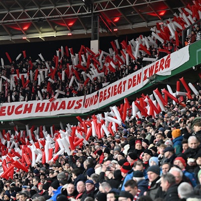 Im Kölner Fanblock hängt ein Spruchband mit der Aufschrift „Wachst über Euch hinaus und besiegt den Zwerg“.