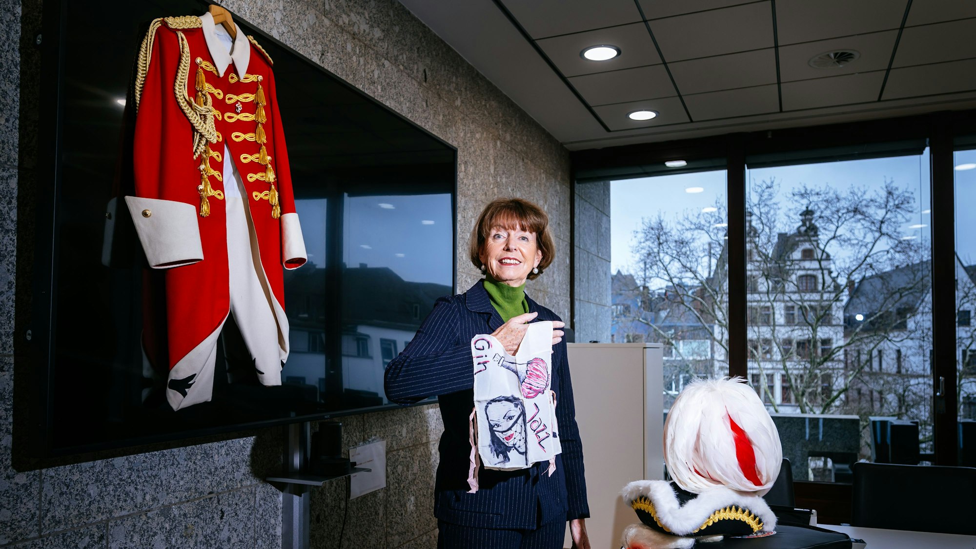 Henriette Reker hält ein selbstgenähtes Kostüm in der Hand. Neben ihr an der Wand hängt eine Uniform.