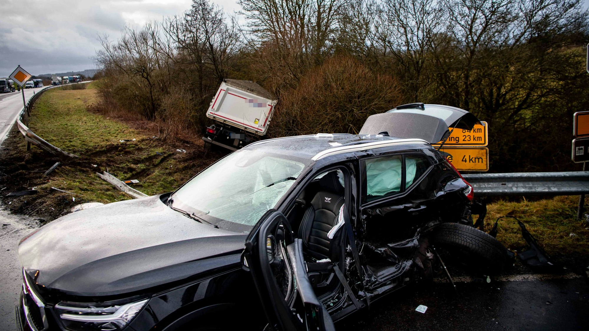Das Bild zeigt ein stark beschädigtes Auto. Im Hintergrund liegt ein Sattelschlepper im Graben.
