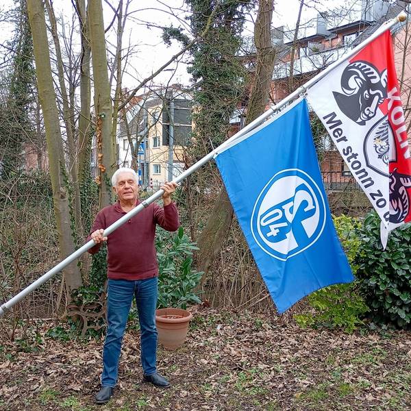 Das Foto zeigt einen Mann mit zwei großen Flaggen an einer Fahnenstange.