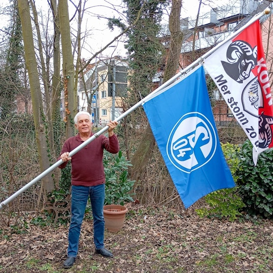 Das Foto zeigt einen Mann mit zwei großen Flaggen an einer Fahnenstange.