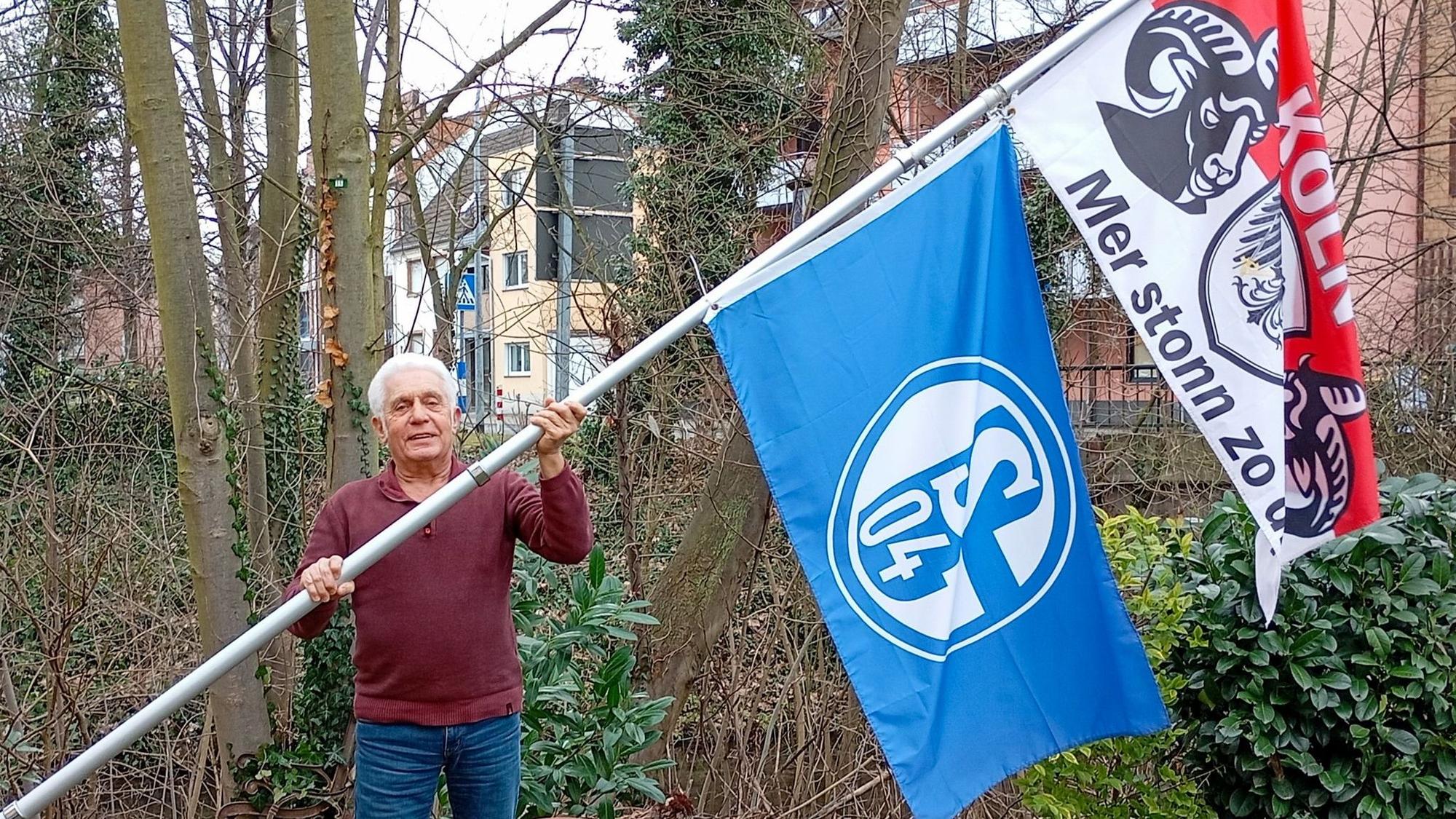 Das Foto zeigt einen Mann mit zwei großen Flaggen an einer Fahnenstange.