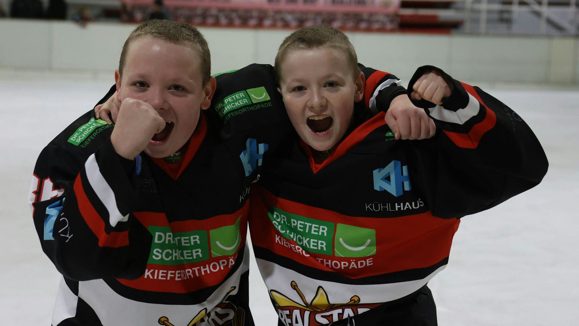 Die Zwillinge Finn und Florian Wolf aus Satzvey tragen Eishockey-Trikots. Mit geballten Fäusten jubeln sie über einen Sieg.