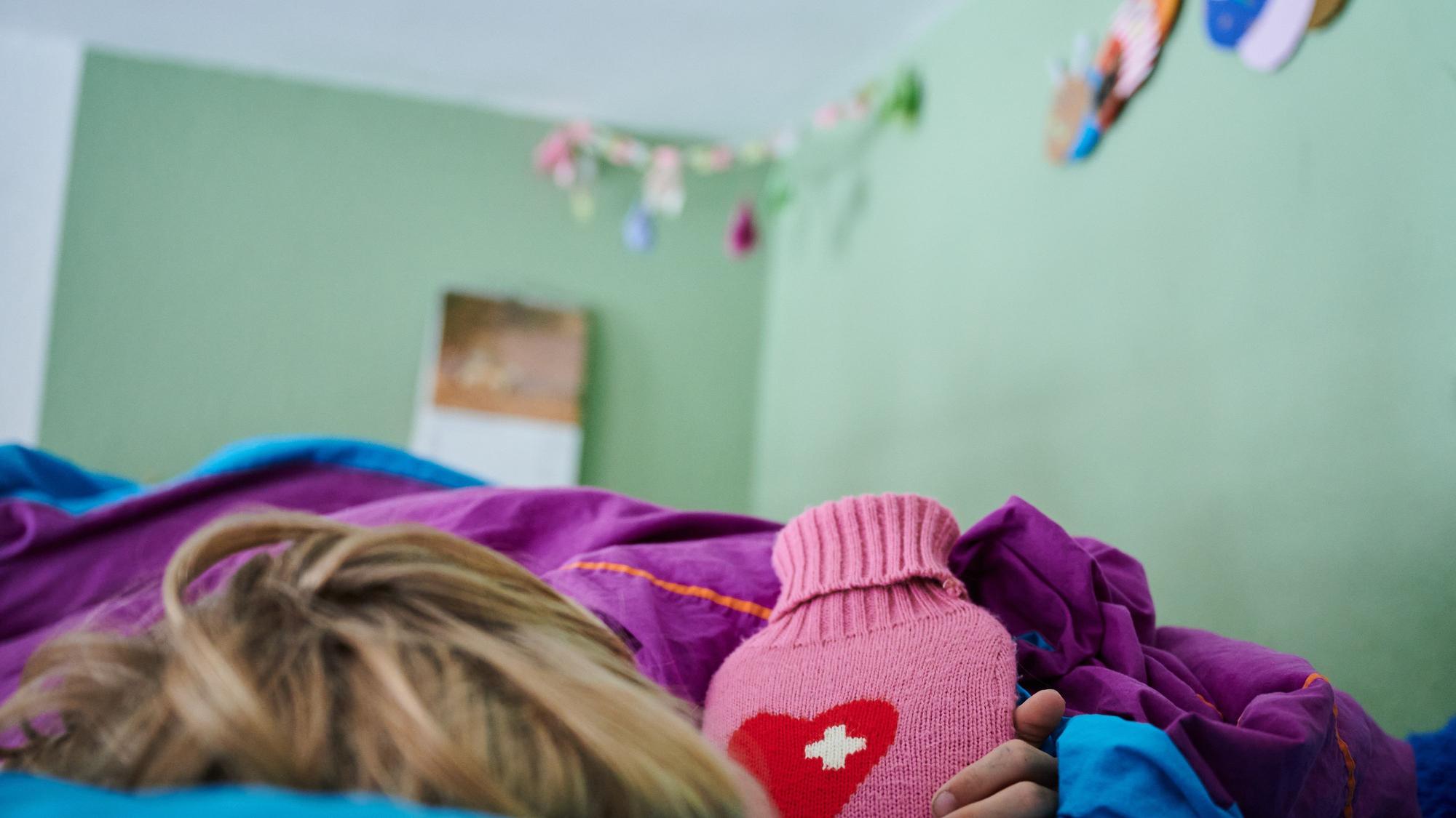 Ein Kind liegt mit einer Wärmflasche im Bett im Kinderzimmer.