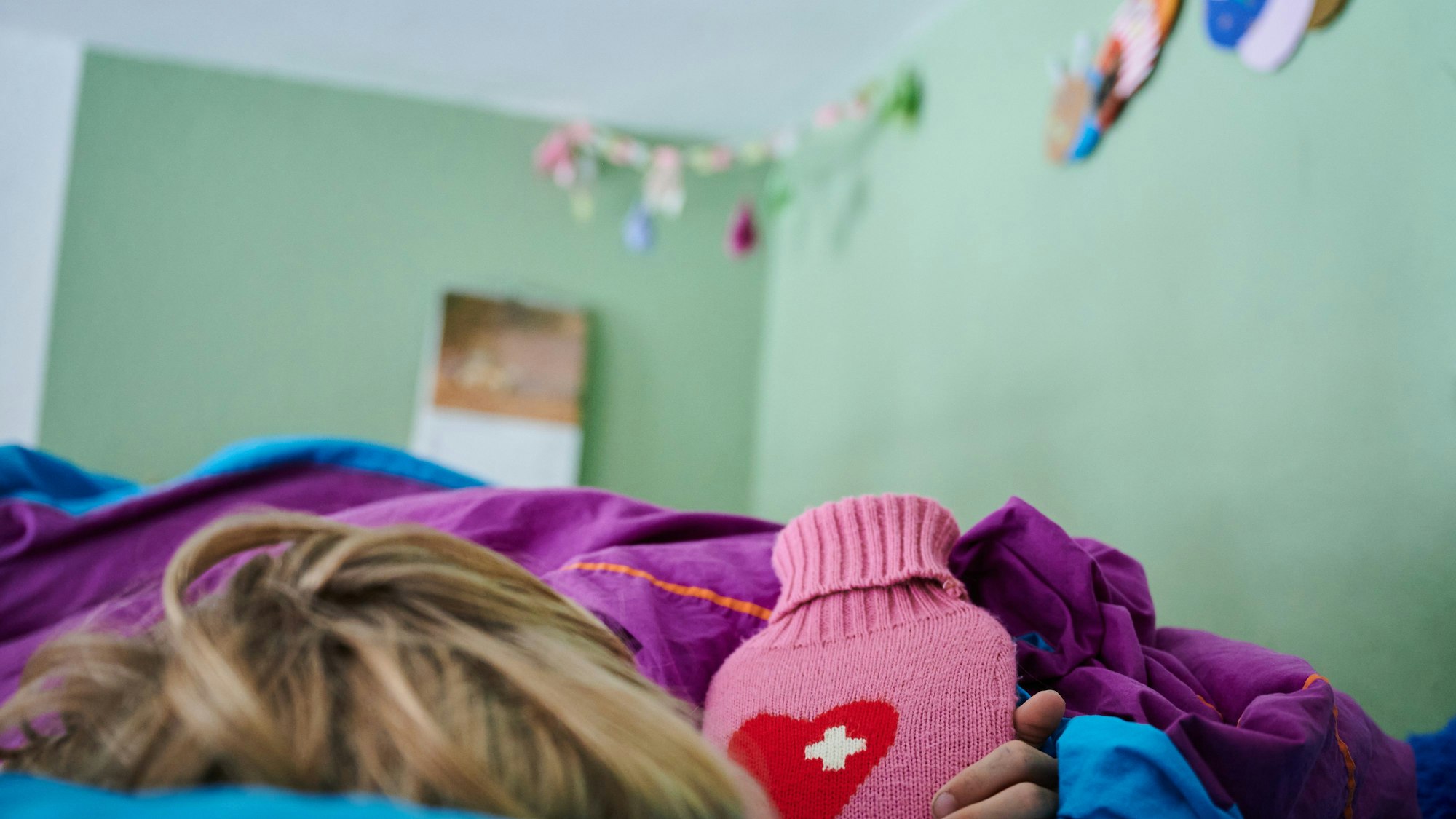 Ein Kind liegt mit einer Wärmflasche im Bett im Kinderzimmer.