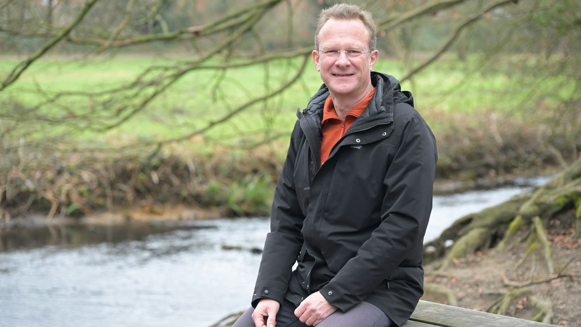 Grünen-Politiker Maik Außendorf sitzt an einem Fluss auf einer Bank.