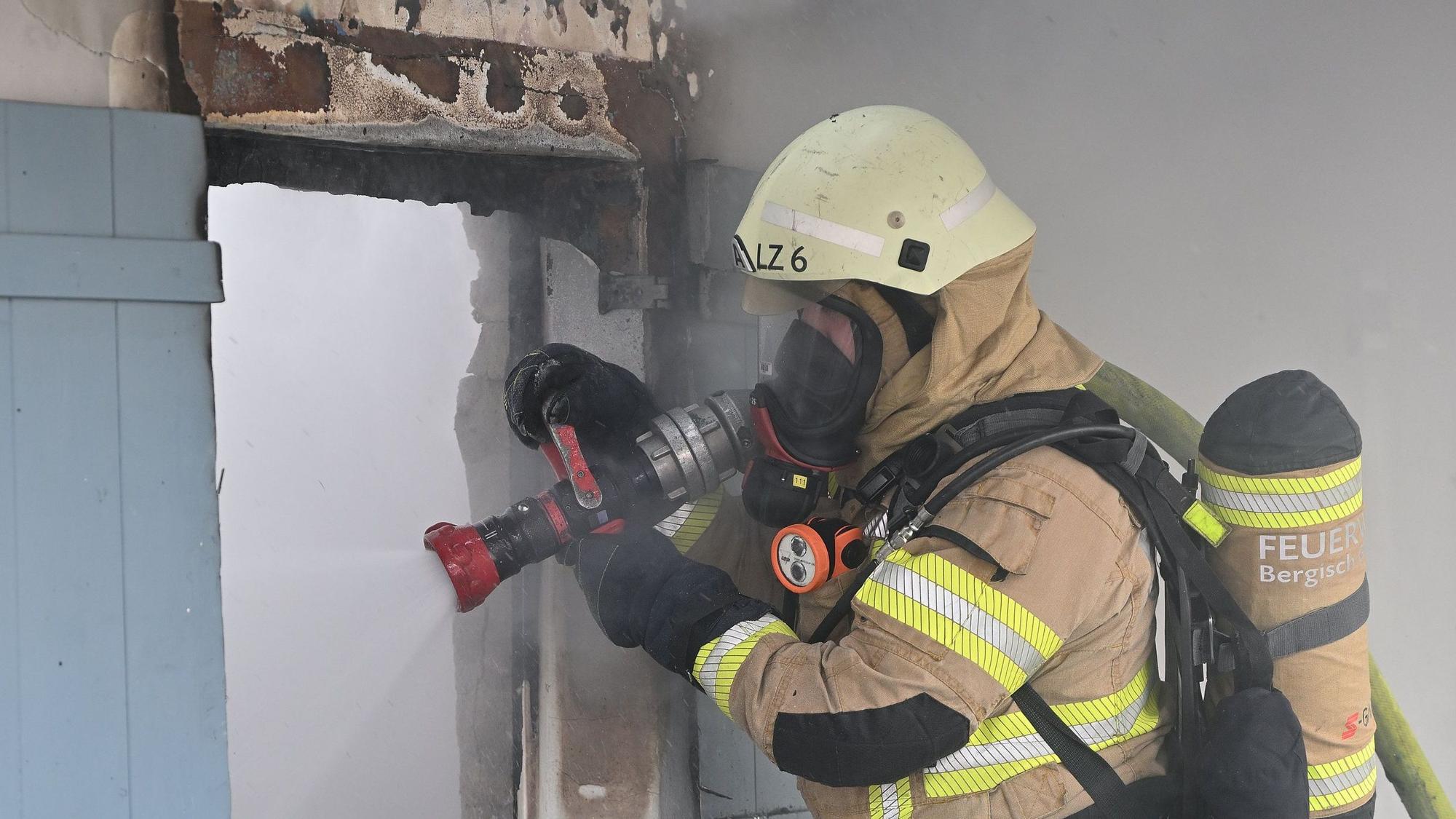 Ein Feuerwehrmann hat einen Schlauch über der Schulter liegen und löscht den damit den Brand.