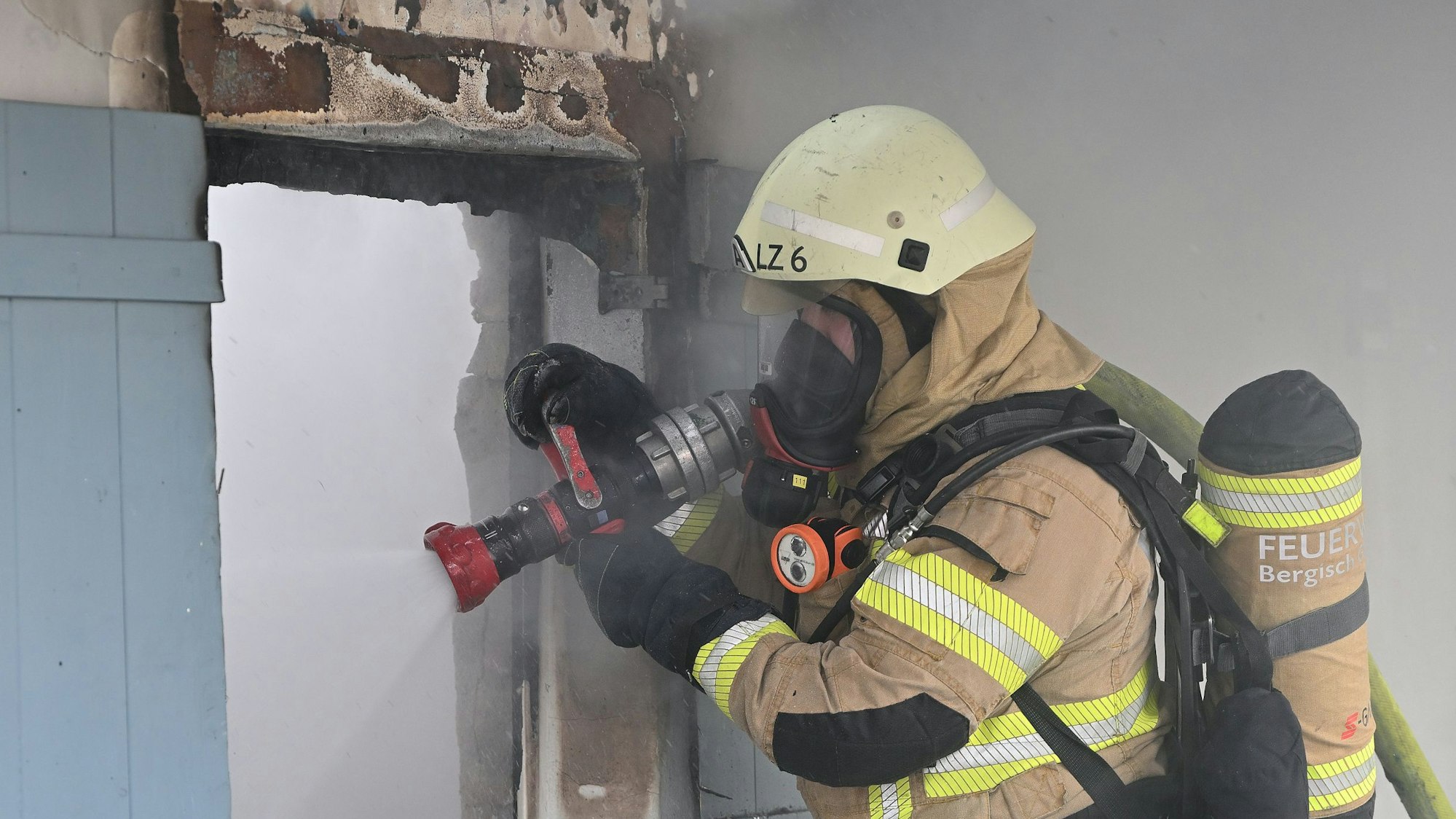 Ein Feuerwehrmann hat einen Schlauch über der Schulter liegen und löscht den damit den Brand.