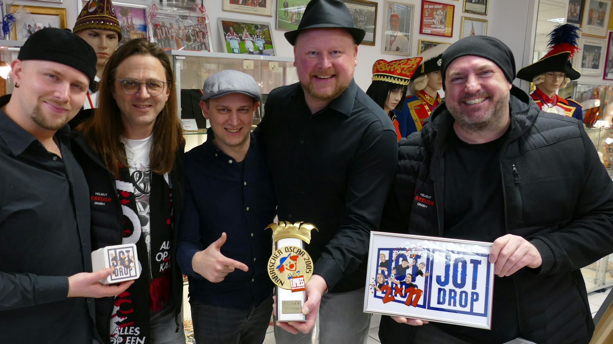Die Bandmitglieder von Jot Drop stehen im Troisdorfer Karnevalsmuseum und präsentieren ihren ersten Närrischen Oscar, den sie dem Museum stiften.