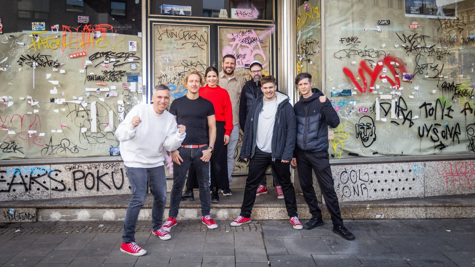 Stehen vor ihrem neuen Ladenlokal: Kasalla-Frontmann Basti Campmann (v.l.), Gitarrist Flo Peil, Managerin Kim Gerstenberg, Gastronom Till Riekenbrauk, Keyboarder Ena Schwiers, Drummer Nils Plum und Bassist Sebi Wagner.