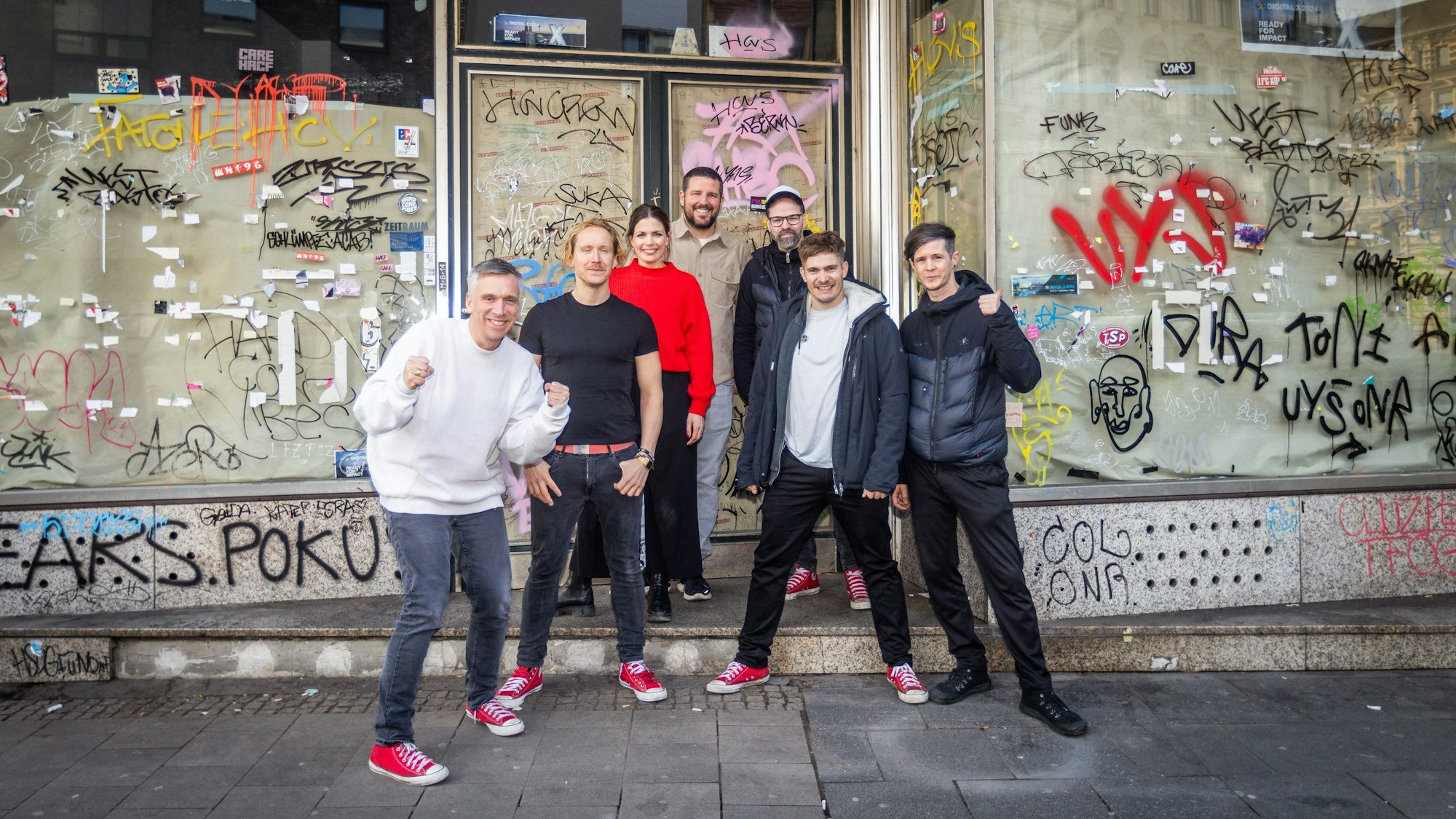 Stehen vor ihrem neuen Ladenlokal: Kasalla-Frontmann Basti Campmann (v.l.), Gitarrist Flo Peil, Managerin Kim Gerstenberg, Gastronom Till Riekenbrauk, Keyboarder Ena Schwiers, Drummer Nils Plum und Bassist Sebi Wagner.