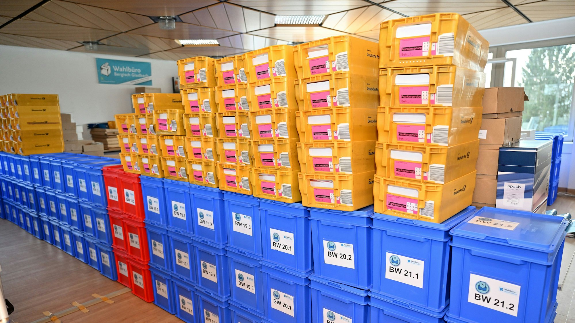 Eine Reihe orangefarbener Kisten steht auf einer Reihe blauer Kisten. Darin befinden sich die Wahlunterlagen.