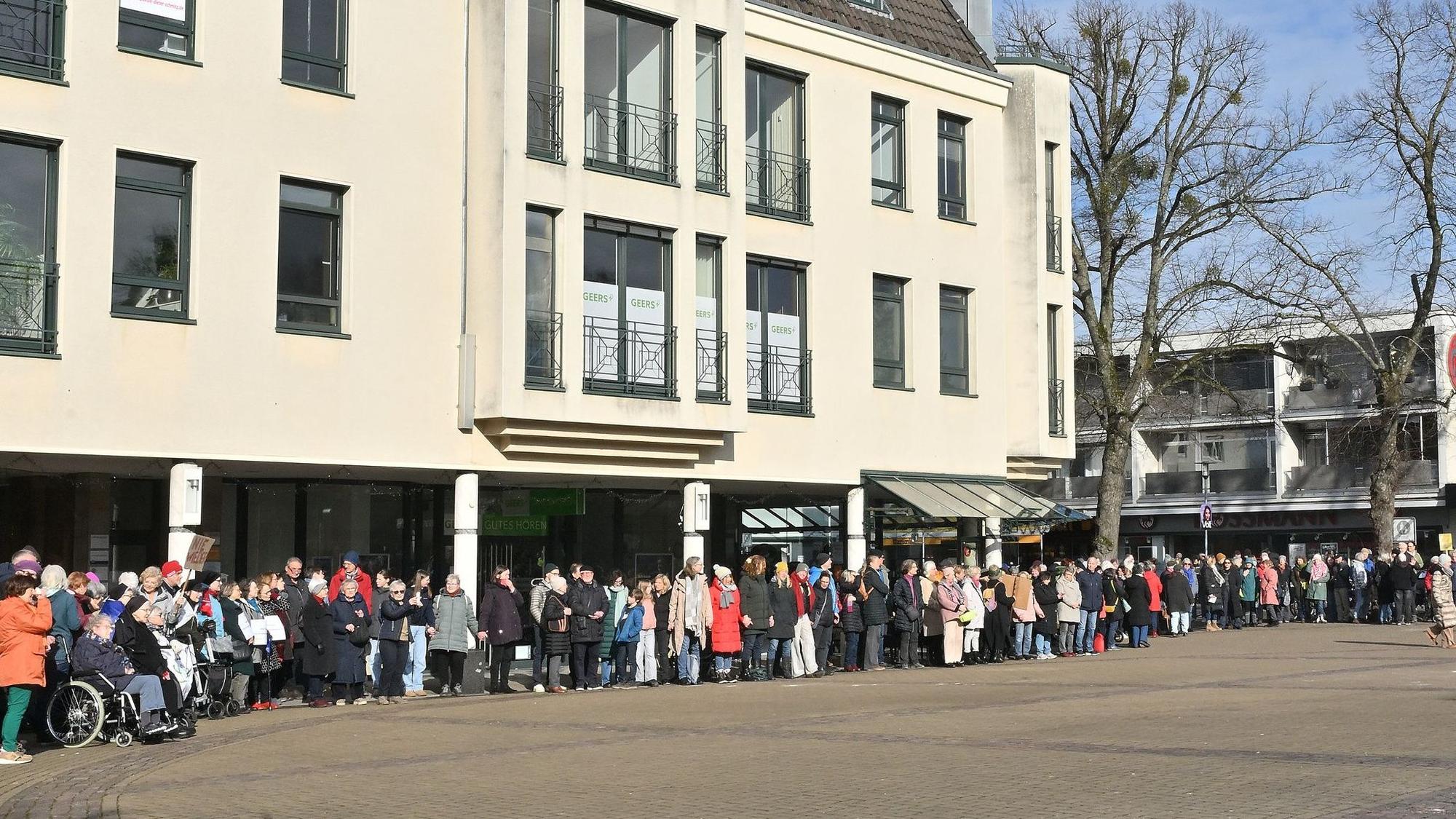 Eine Reihe von Menschen steht vor einem Haus und setzt damit ein Zeichen gegen Rassismus und für Demokratie.