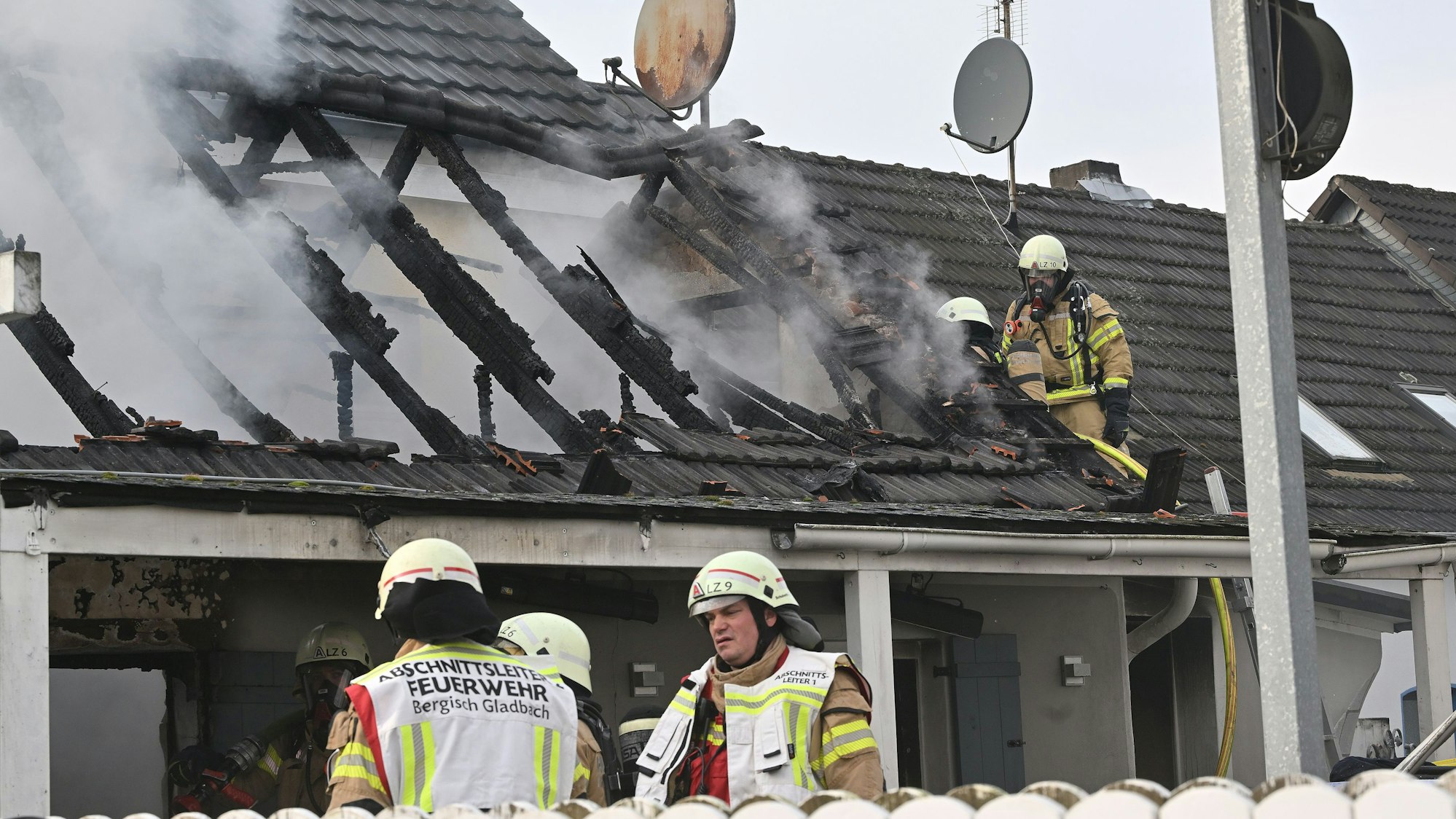 Feuerwehrleute stehen vor einer rauchenden Brandruine in Bergisch Gladbach.
