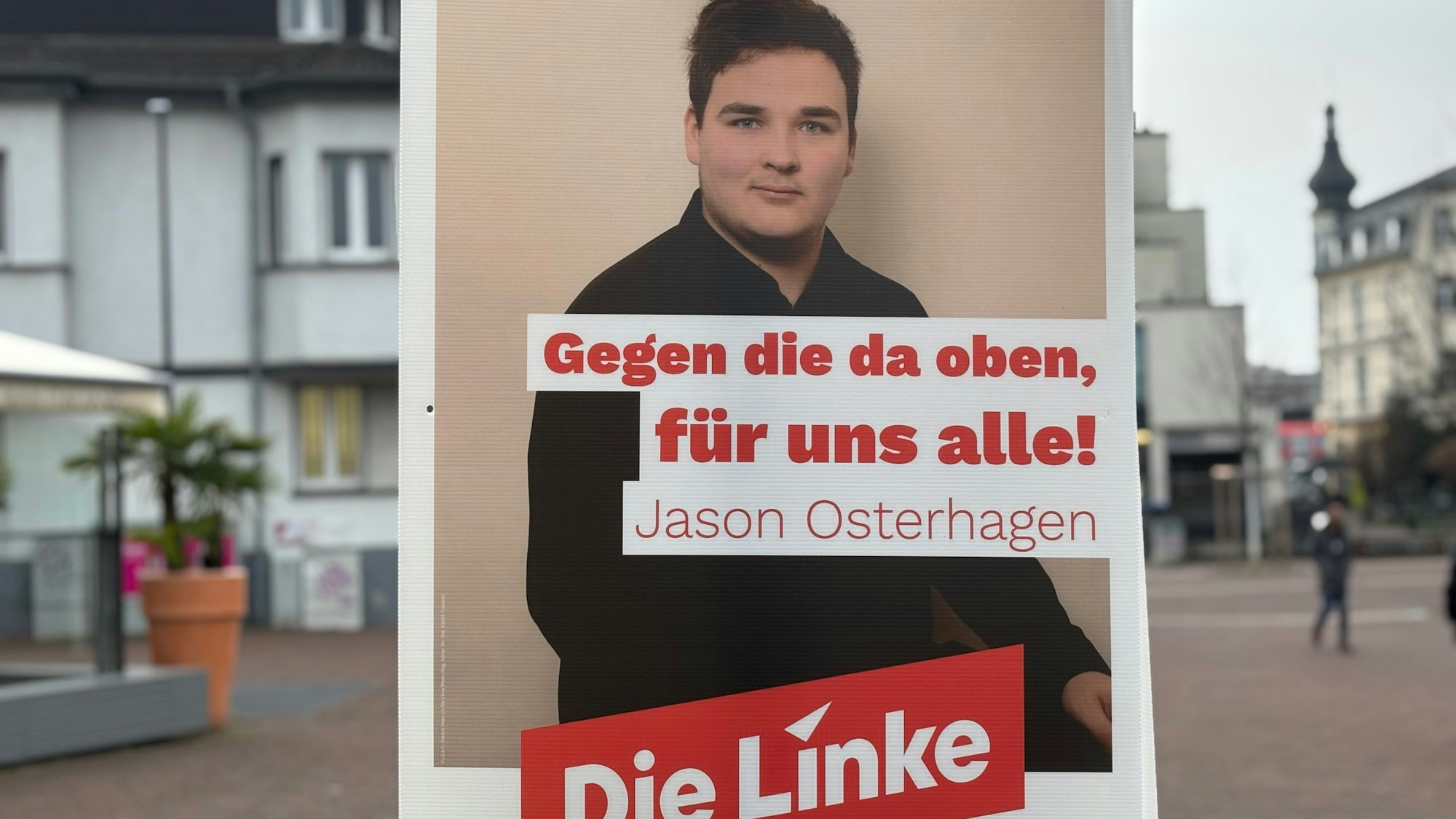 Auf einem Wahlplakat der Partei Die Linke stehen ein junger Mann und der Satz „Gegen die da oben, für uns alle!“.