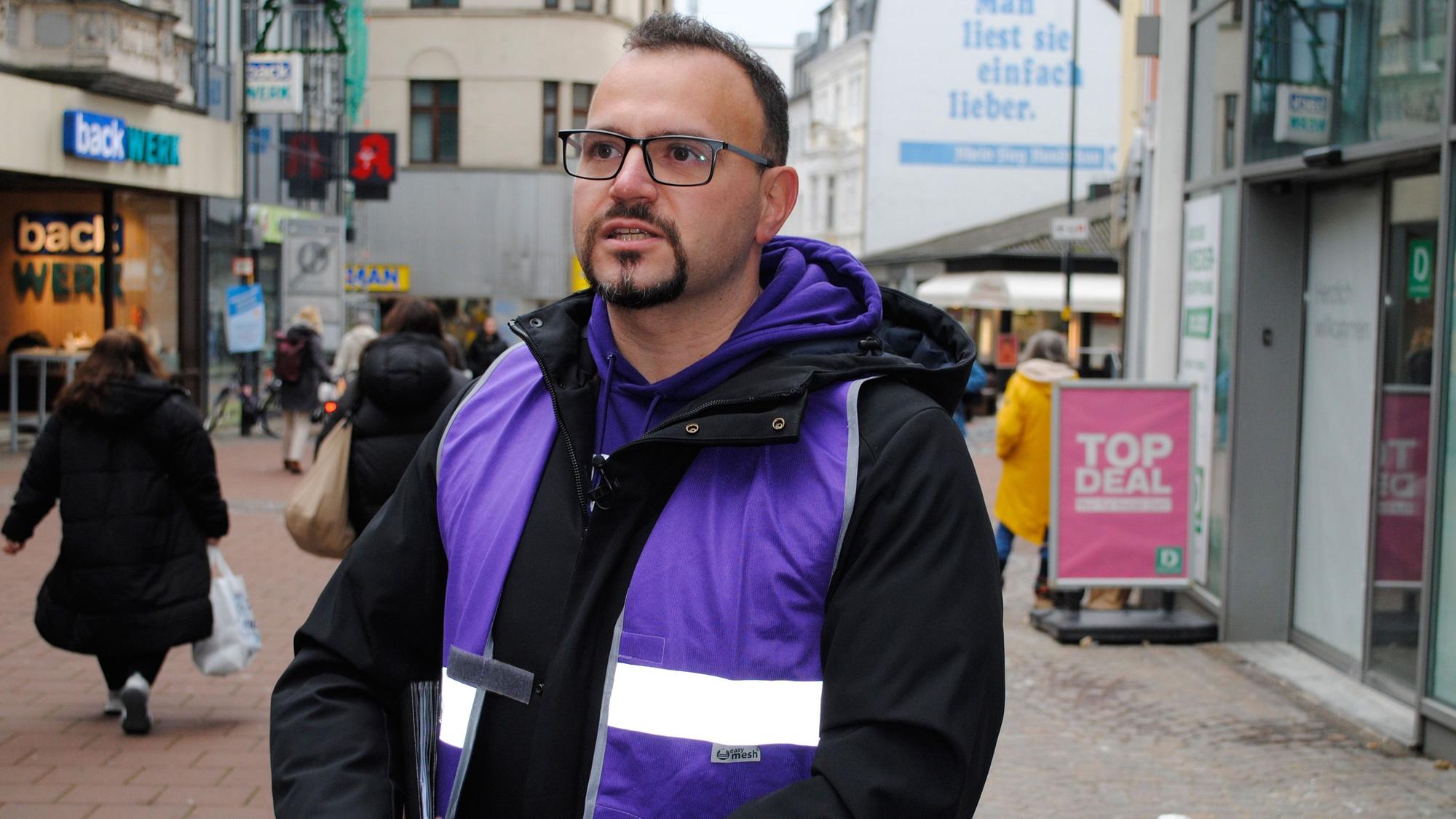 Ein Mann mit Brille und Jacke steht in der Fußgängerzone von Siegburg.