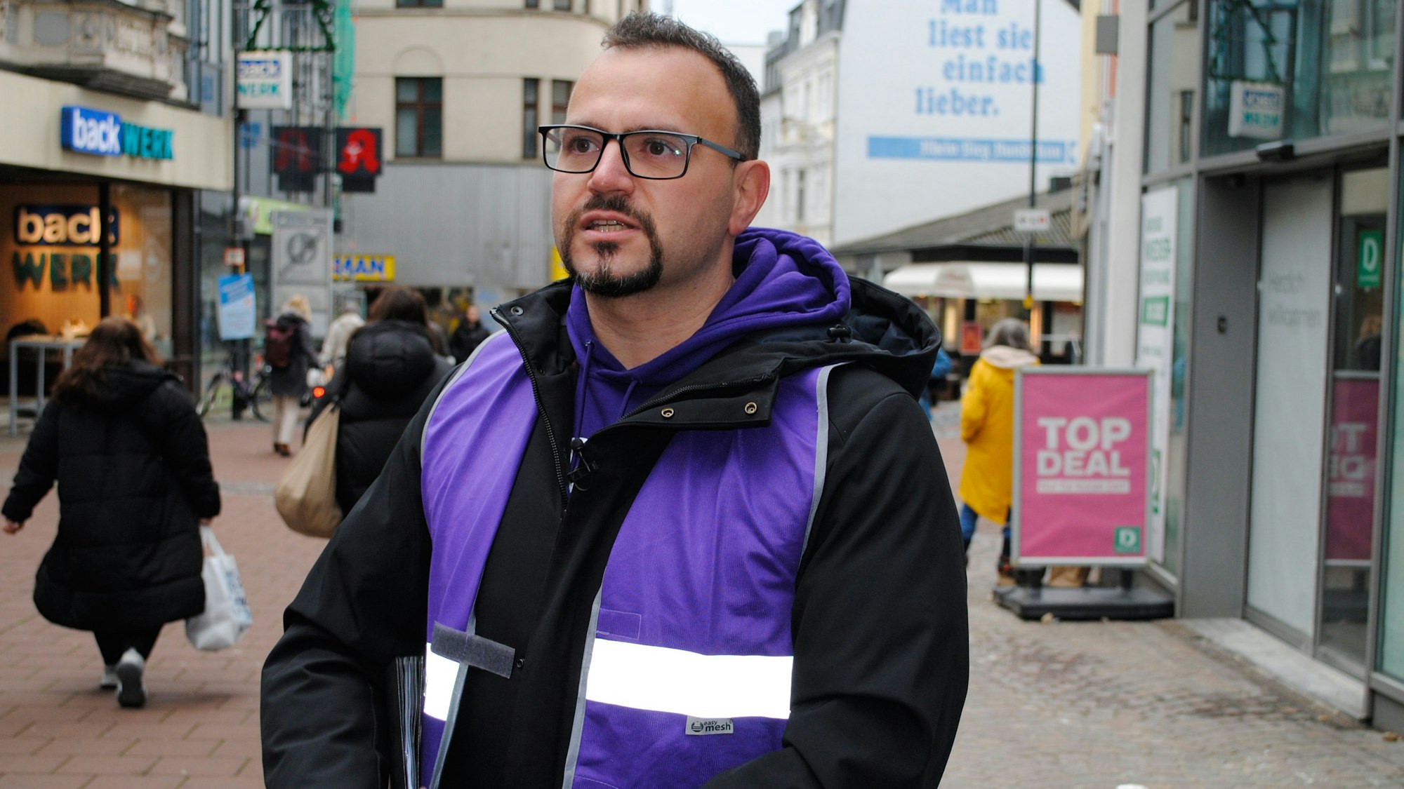 Ein Mann mit Brille und Jacke steht in der Fußgängerzone von Siegburg.