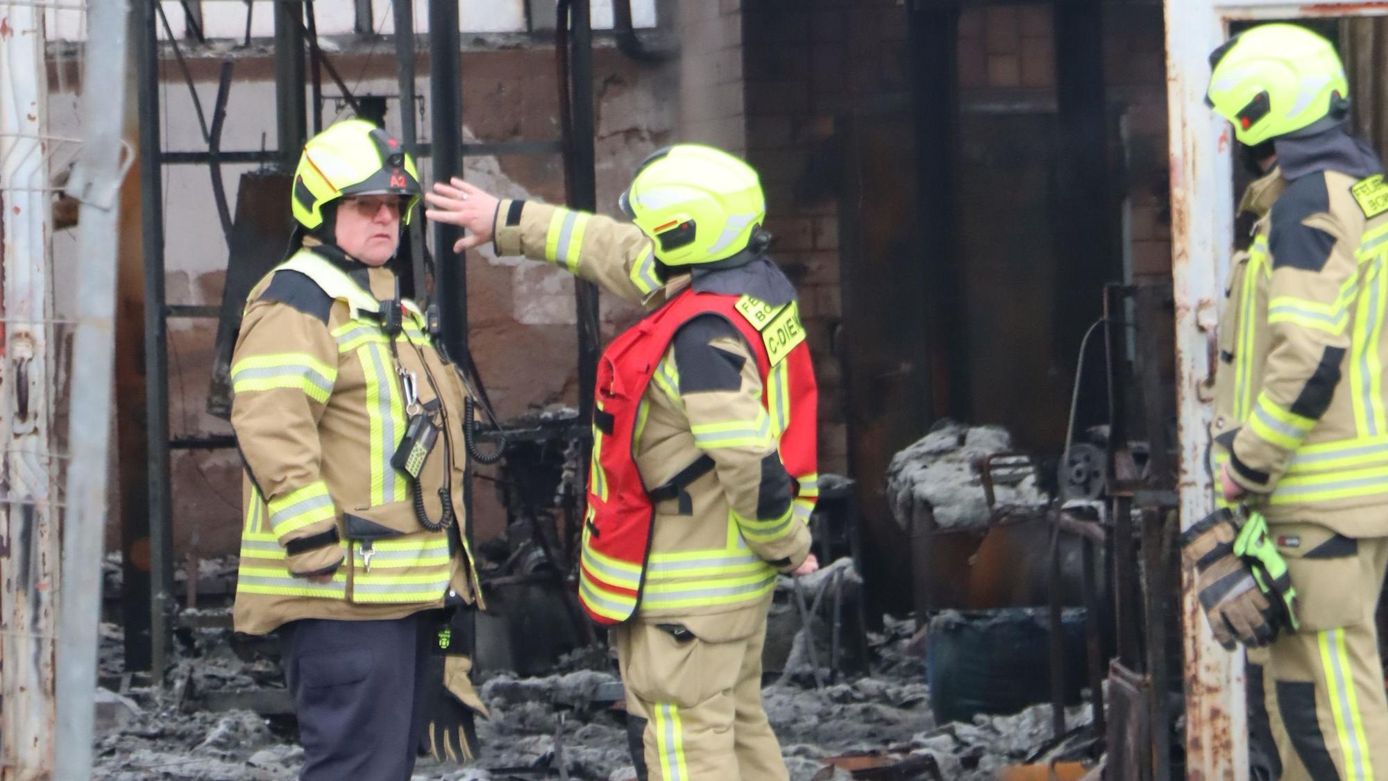 Feuerwehrleute am Halleneingang. Noch kann zur Brandursache nichts gesagt werden.